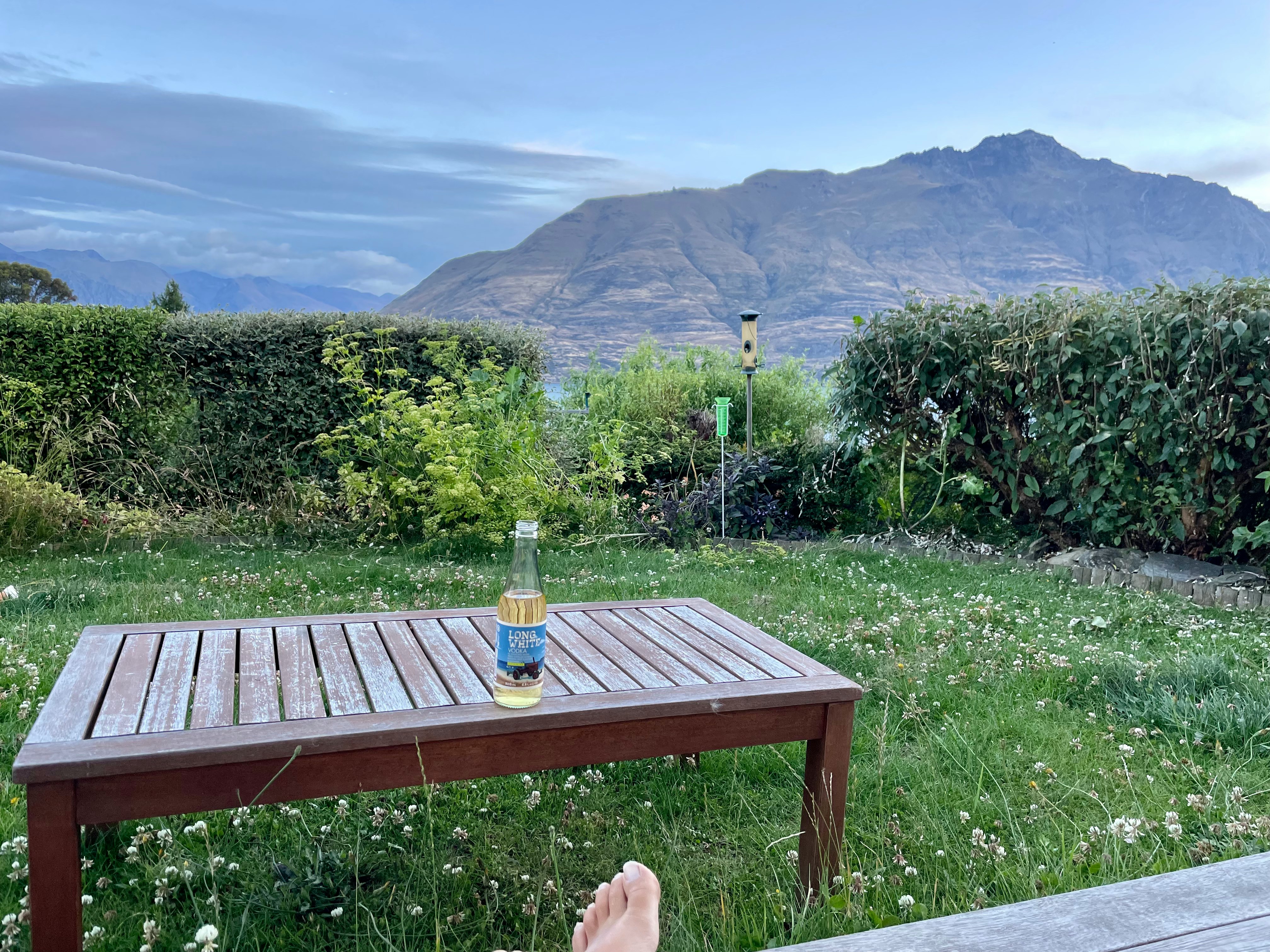 mesa de madera sobre césped de jardín con botella y flores