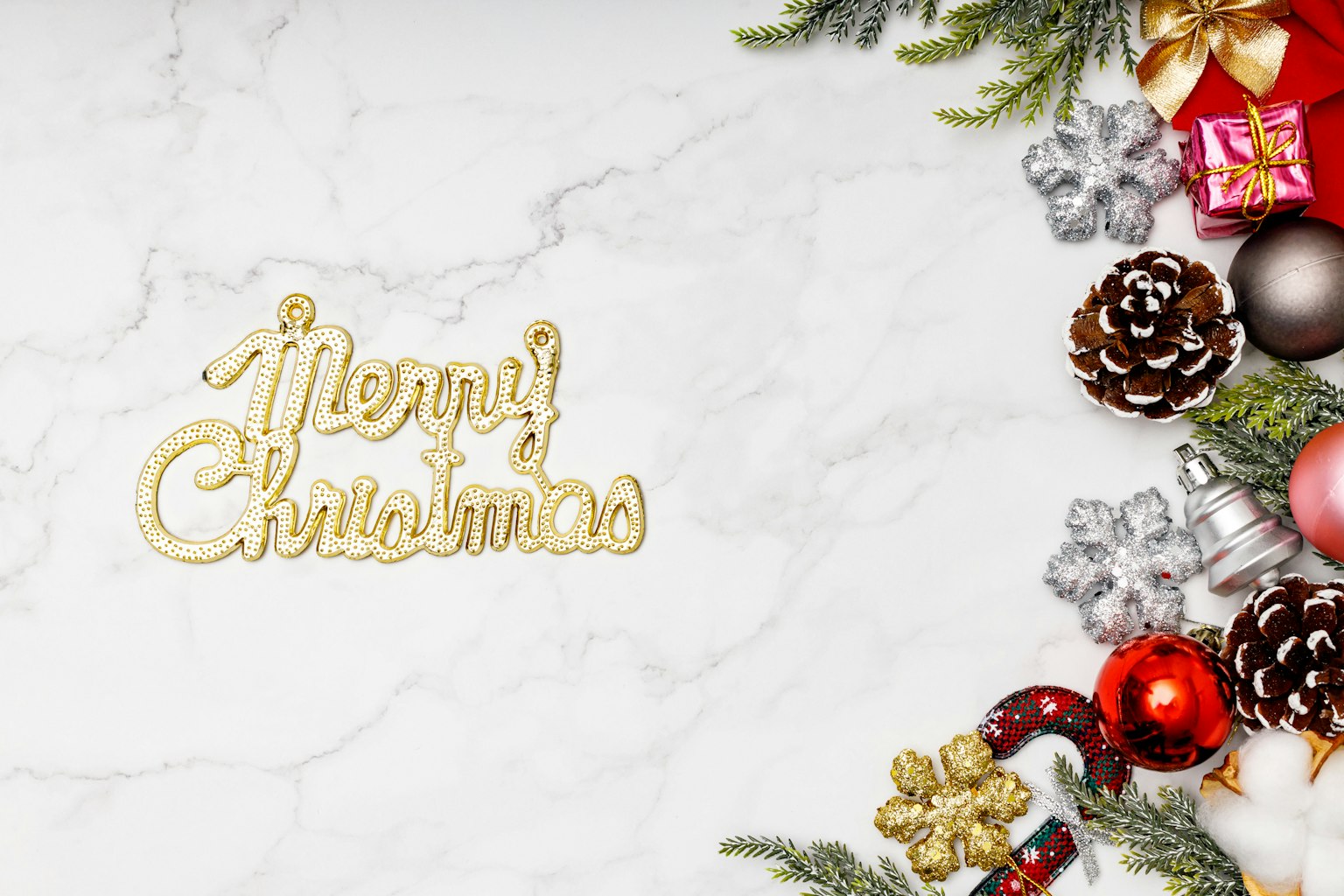 Testo dorato Buon Natale su uno sfondo in marmo bianco con ornamenti rossi e pigne