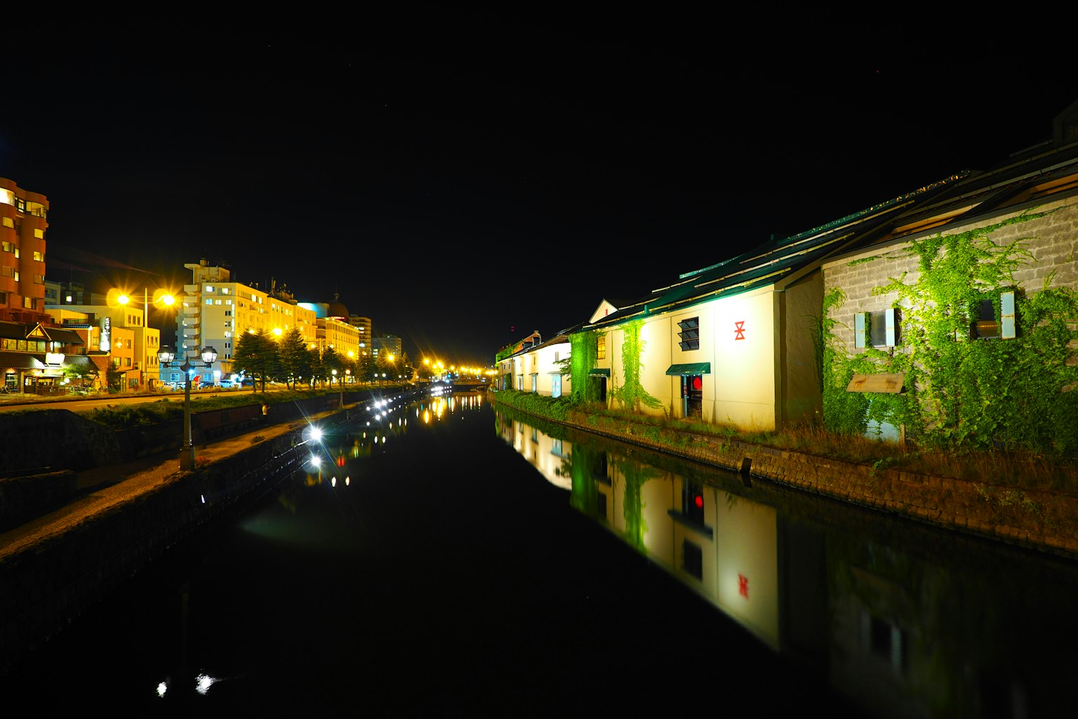 Vista nocturna de edificios a lo largo de un canal con reflejos de farolas en el agua