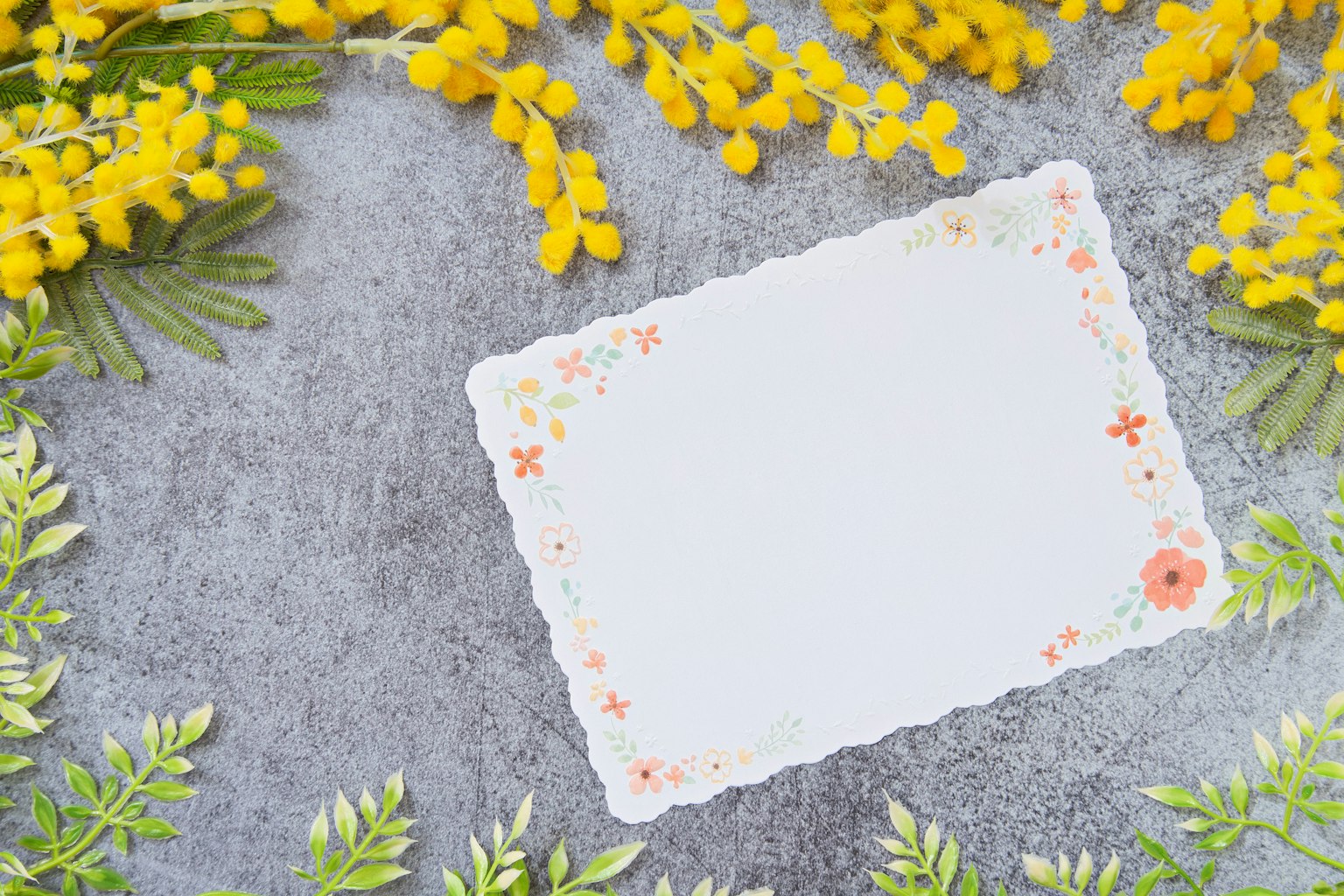 Ein weißes Notizblatt umgeben von gelben Blumen und grünen Blättern