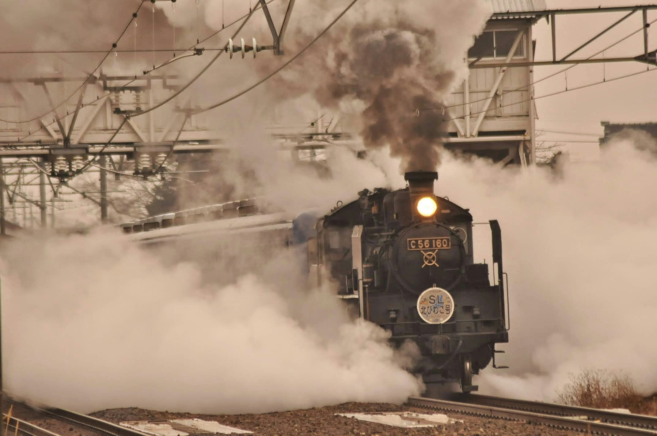 蒸気機関車が白い煙を上げて走る鉄道風景