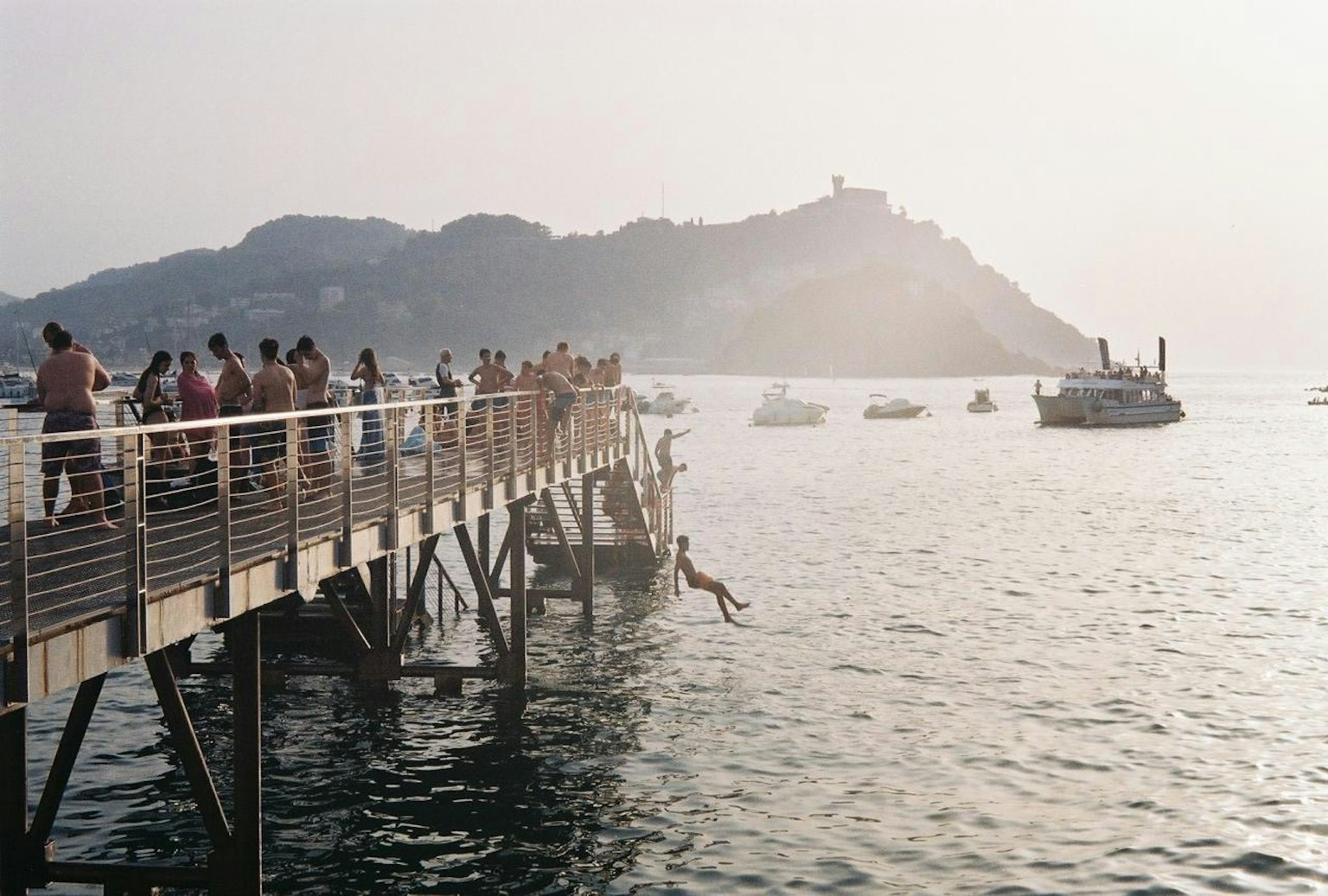 人々が桟橋に集まり、海に飛び込む様子が見える風景