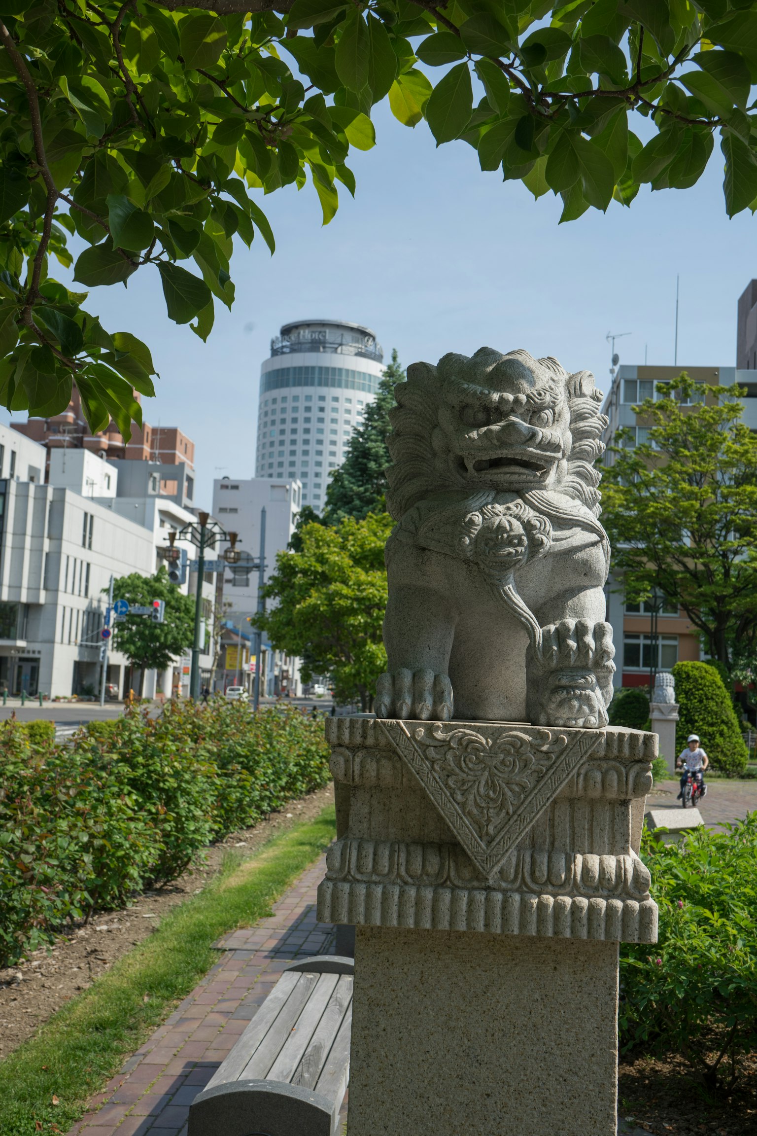 Statue de lion en pierre dans un parc avec des bâtiments modernes en arrière-plan