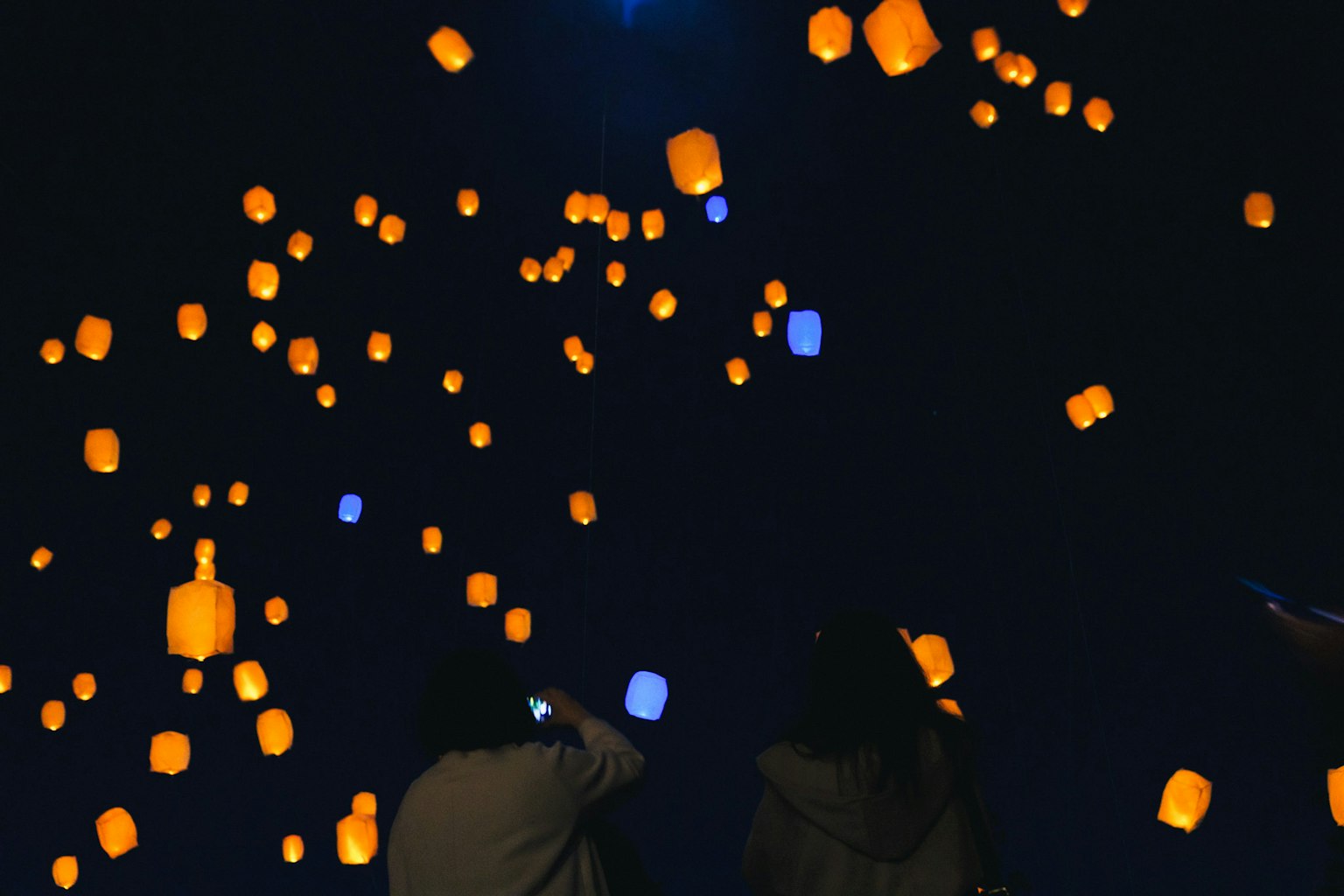 Des personnes regardant des lanternes orange et bleues flotter dans le ciel nocturne