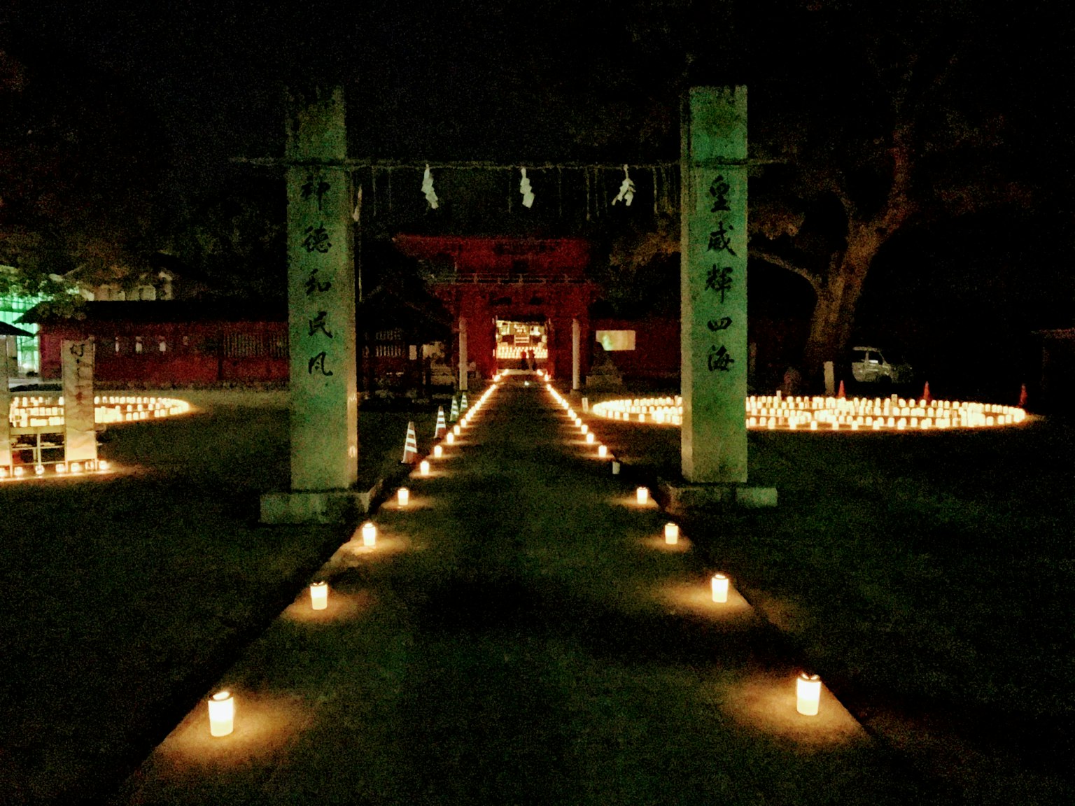 Chemin éclairé par des bougies menant à un sanctuaire la nuit avec des portes torii en pierre