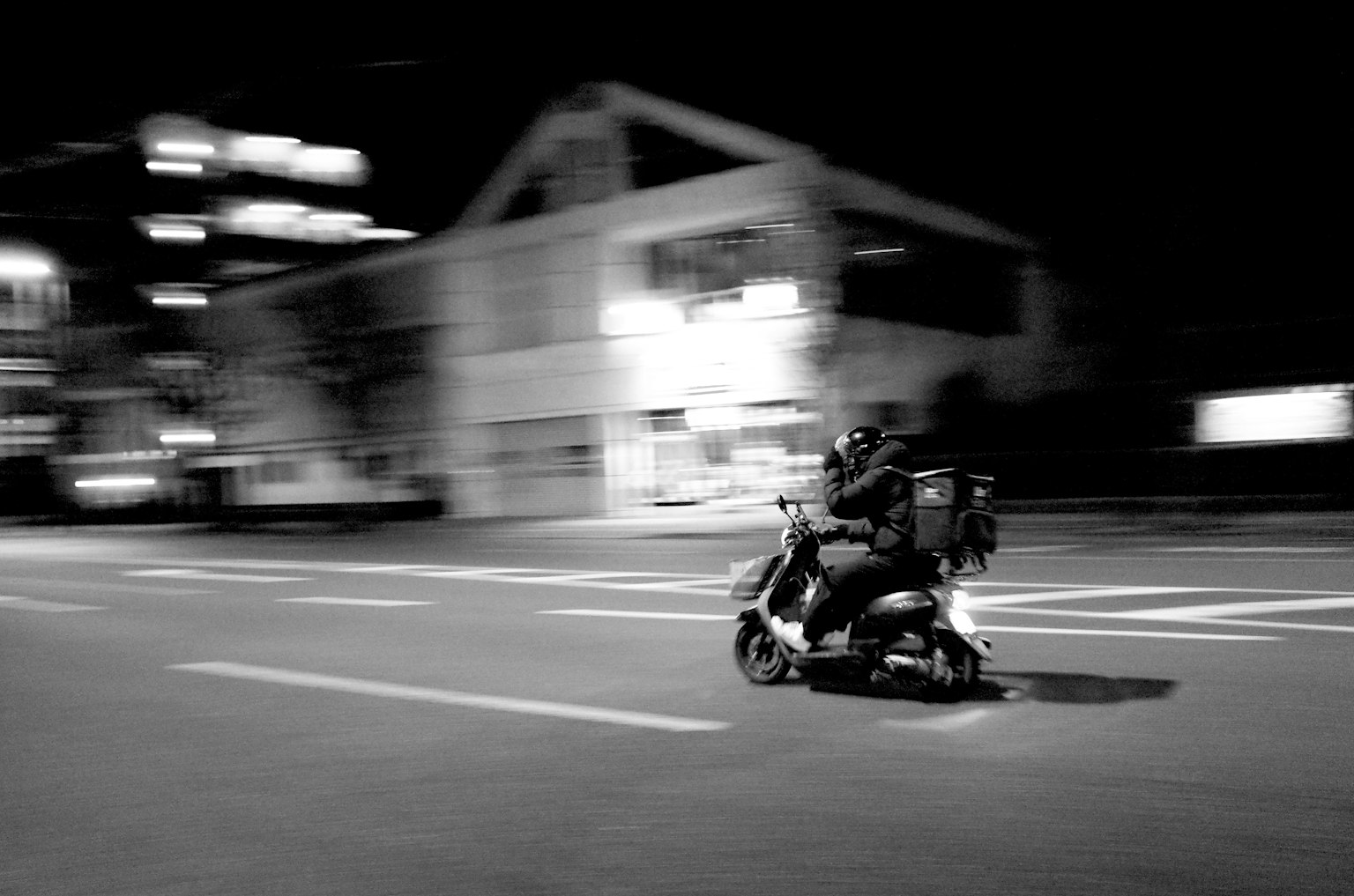 Deux personnes sur un scooter filant à travers une ville la nuit