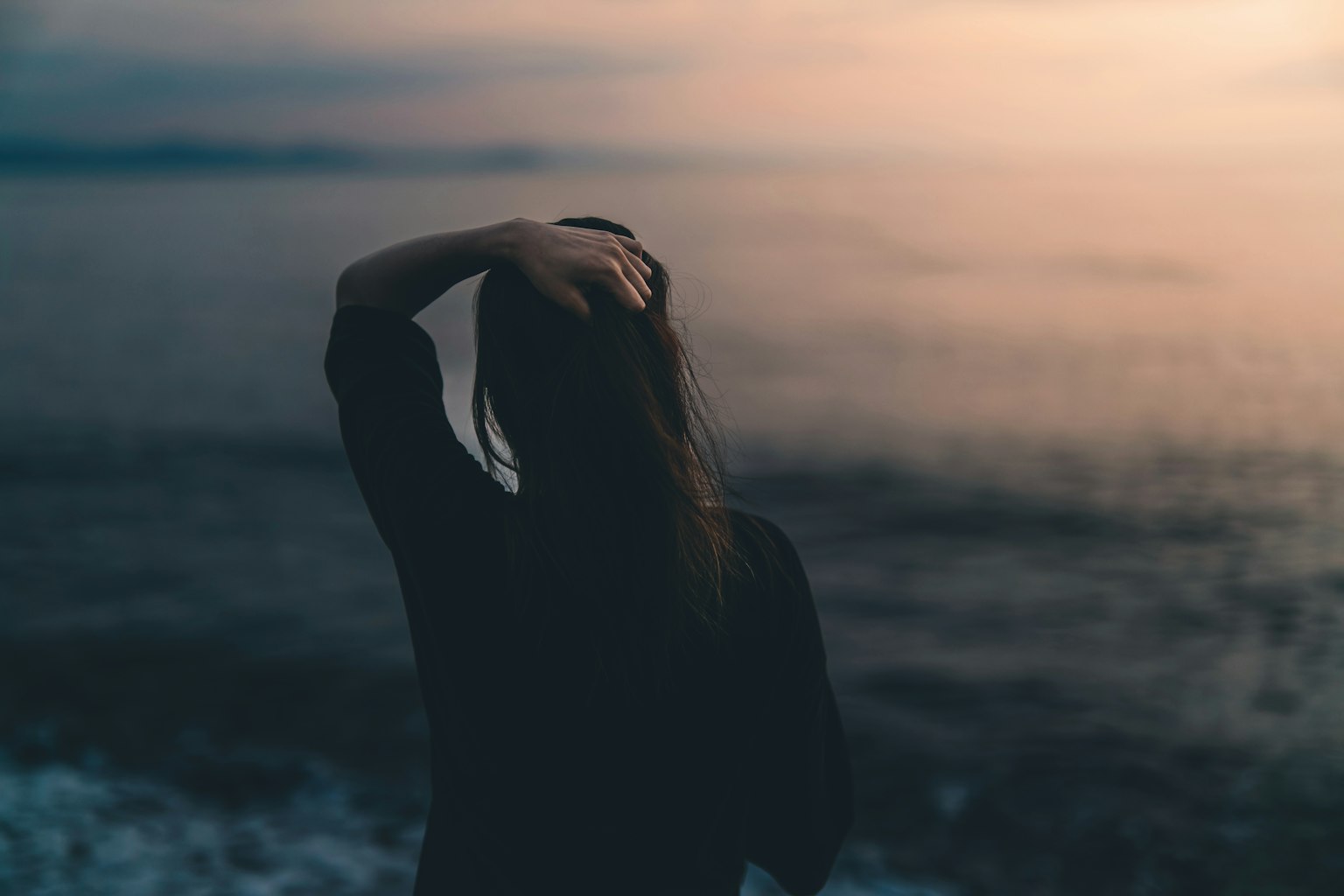 Silhouette di una donna che si trova di fronte all'oceano al crepuscolo