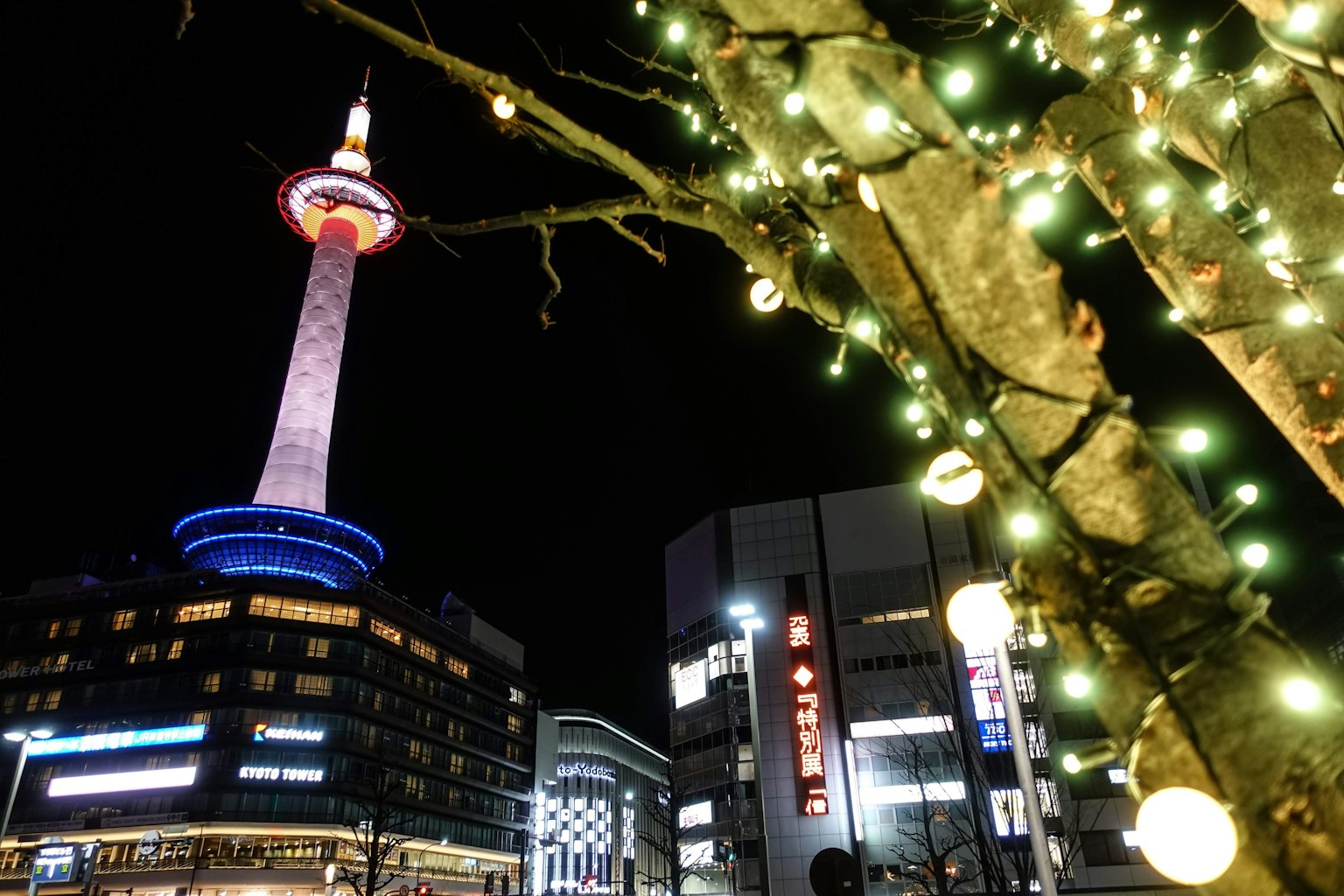 Torre de Kioto iluminada por la noche con luces decorativas en un árbol