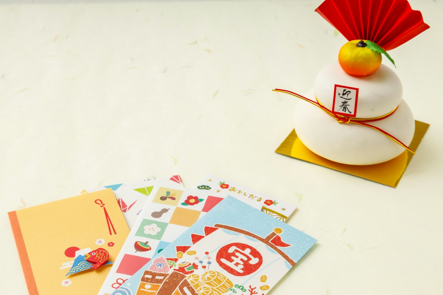 Una decorazione di Capodanno con un dolce di riso bianco con un ornamento rosso e un mandarino sopra, insieme a carte colorate