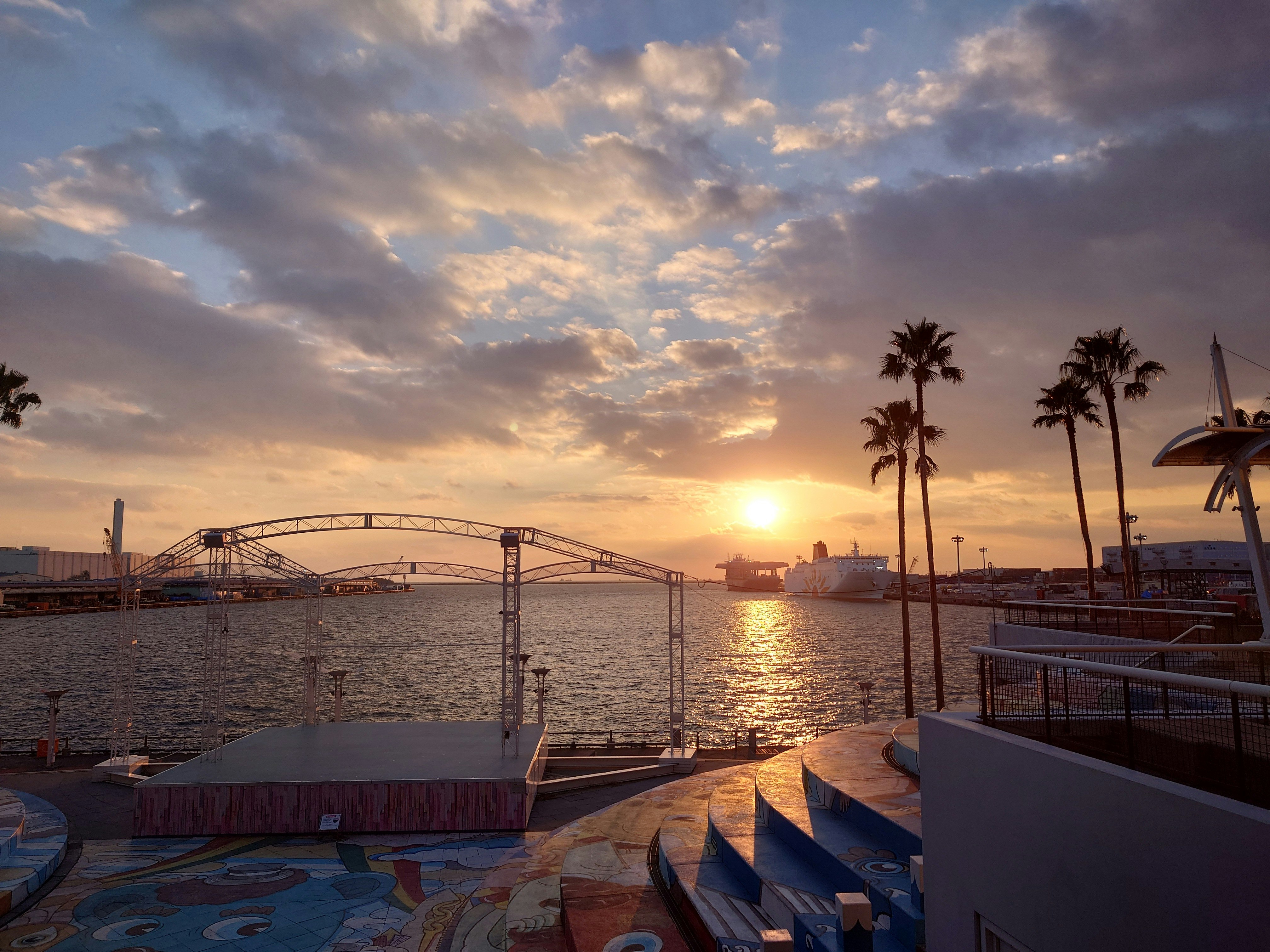夕日に照らされた海沿いの桟橋とヤシの木の並ぶ景色