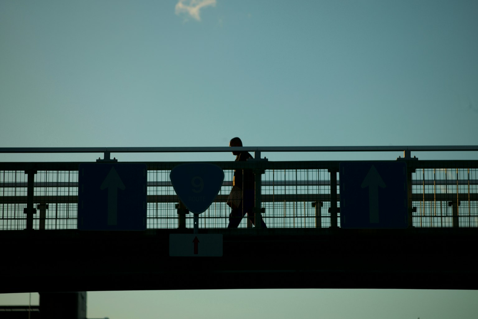 Silhouette of a person walking on a bridge under a blue sky