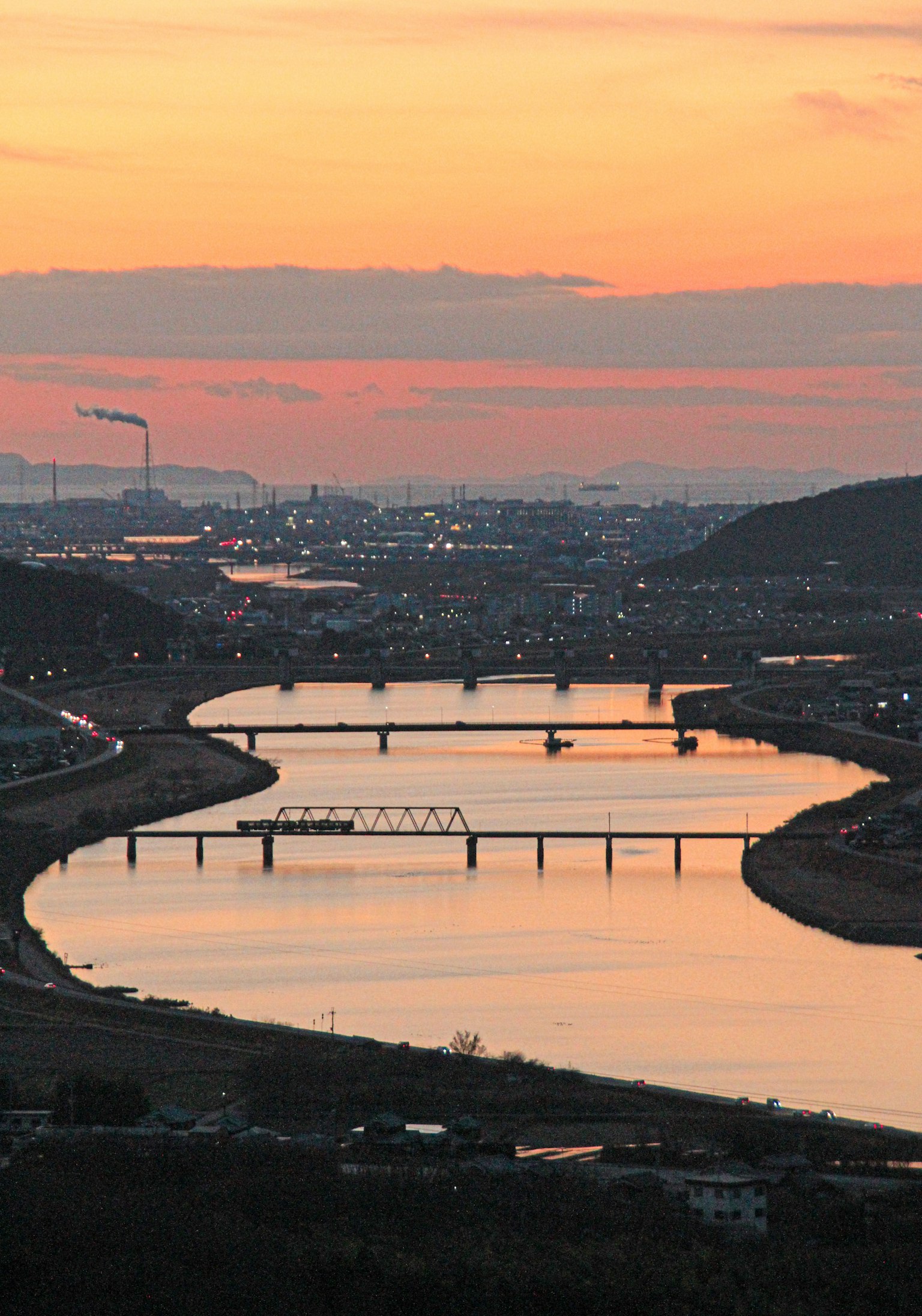 Vista panoramica di un fiume che riflette un cielo al tramonto con ponti e silhouette di città