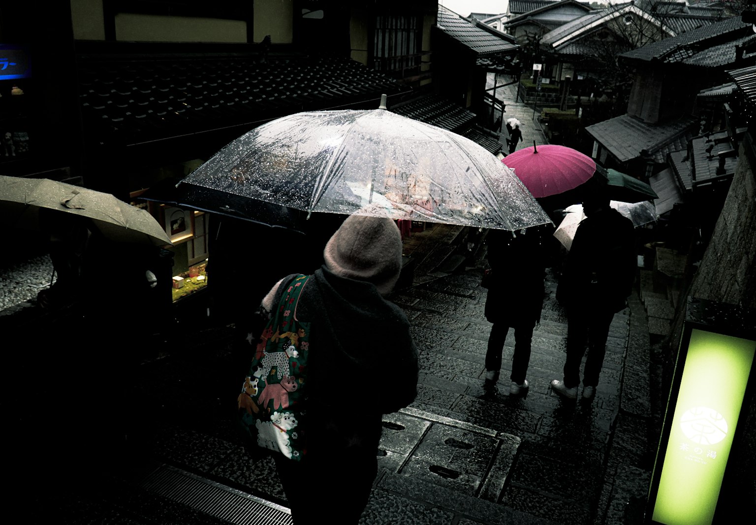 Street scene with people walking under colorful umbrellas in the rain