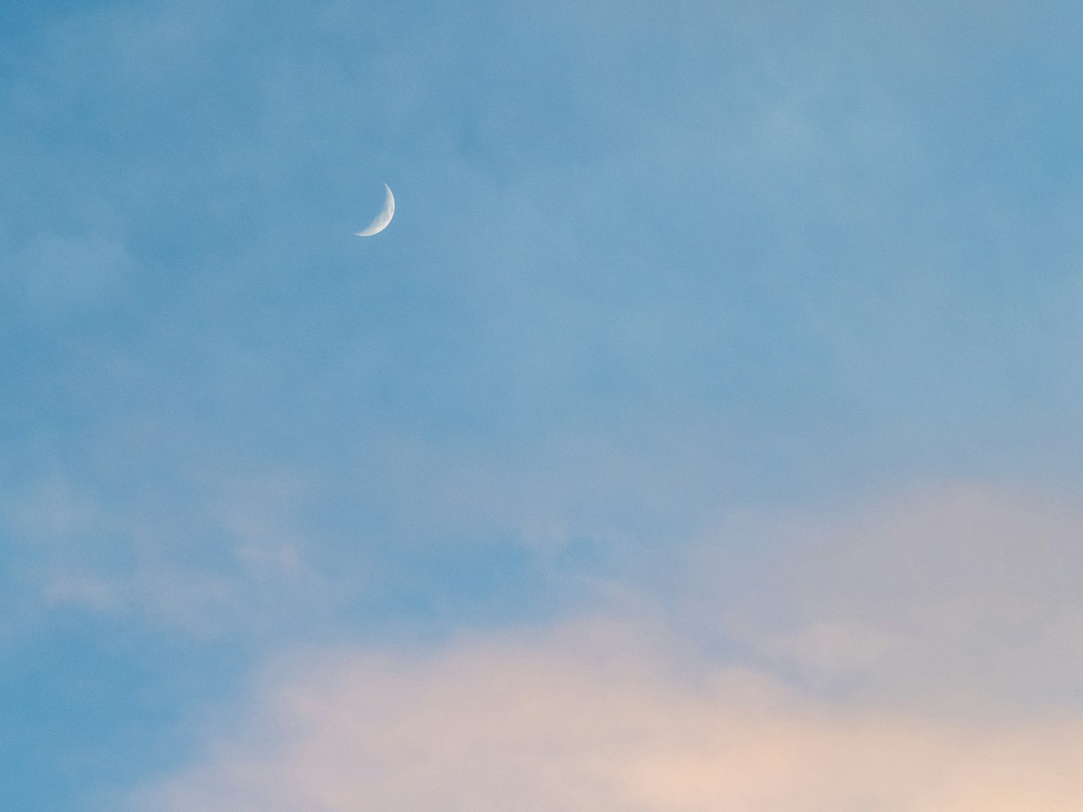 Luna creciente delgada en un cielo azul con nubes suaves