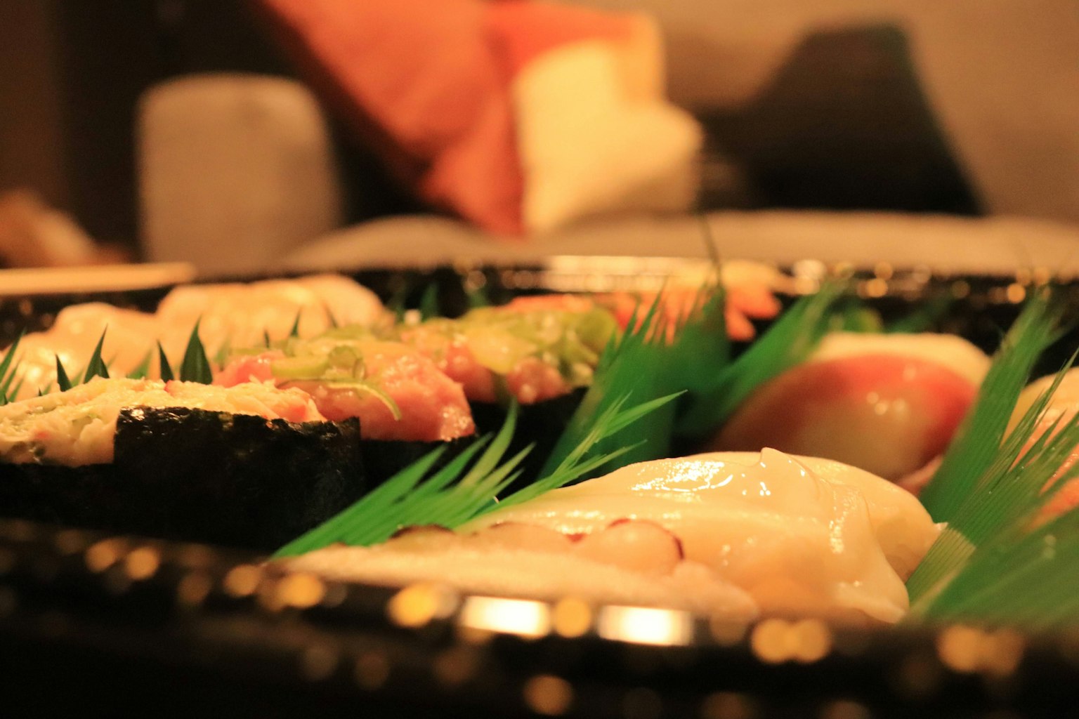 Một đĩa sushi được bày trên lá xanh trong không gian ấm cúng