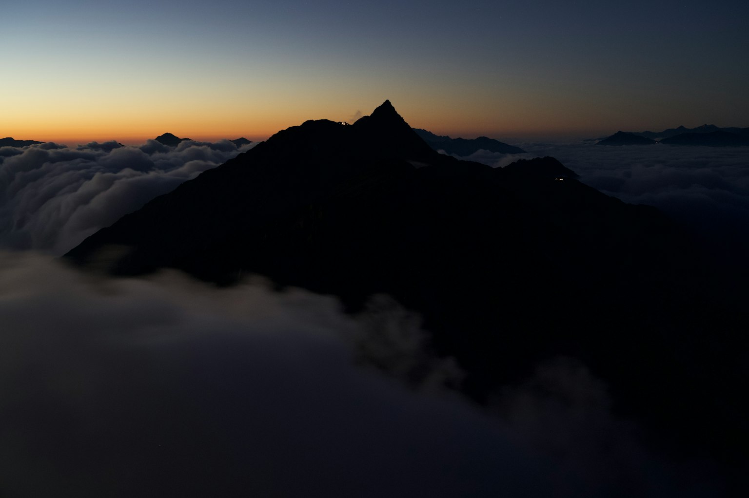 Silhouette di una montagna che emerge dalle nuvole al tramonto