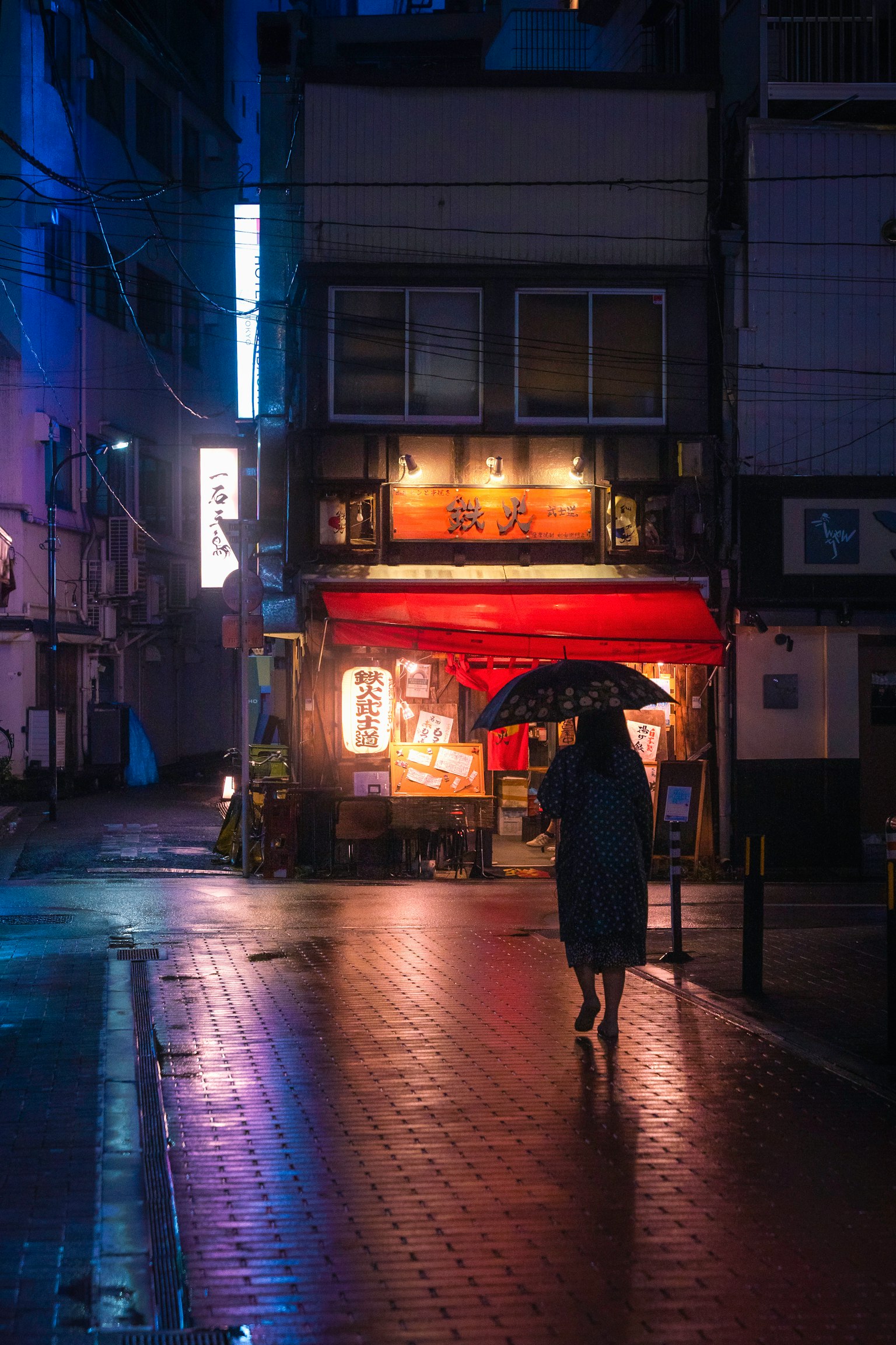 一個人撐著傘走在被霓虹燈照亮的雨天街道上