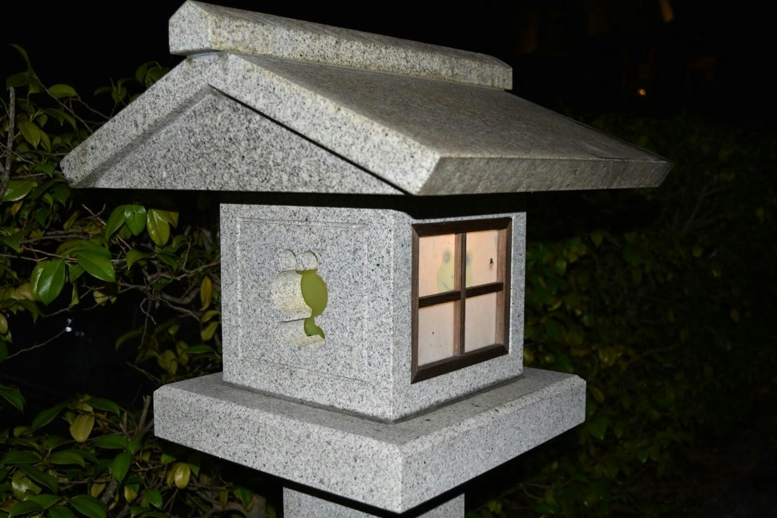 Stone lantern illuminated at night with detailed windows and green decoration