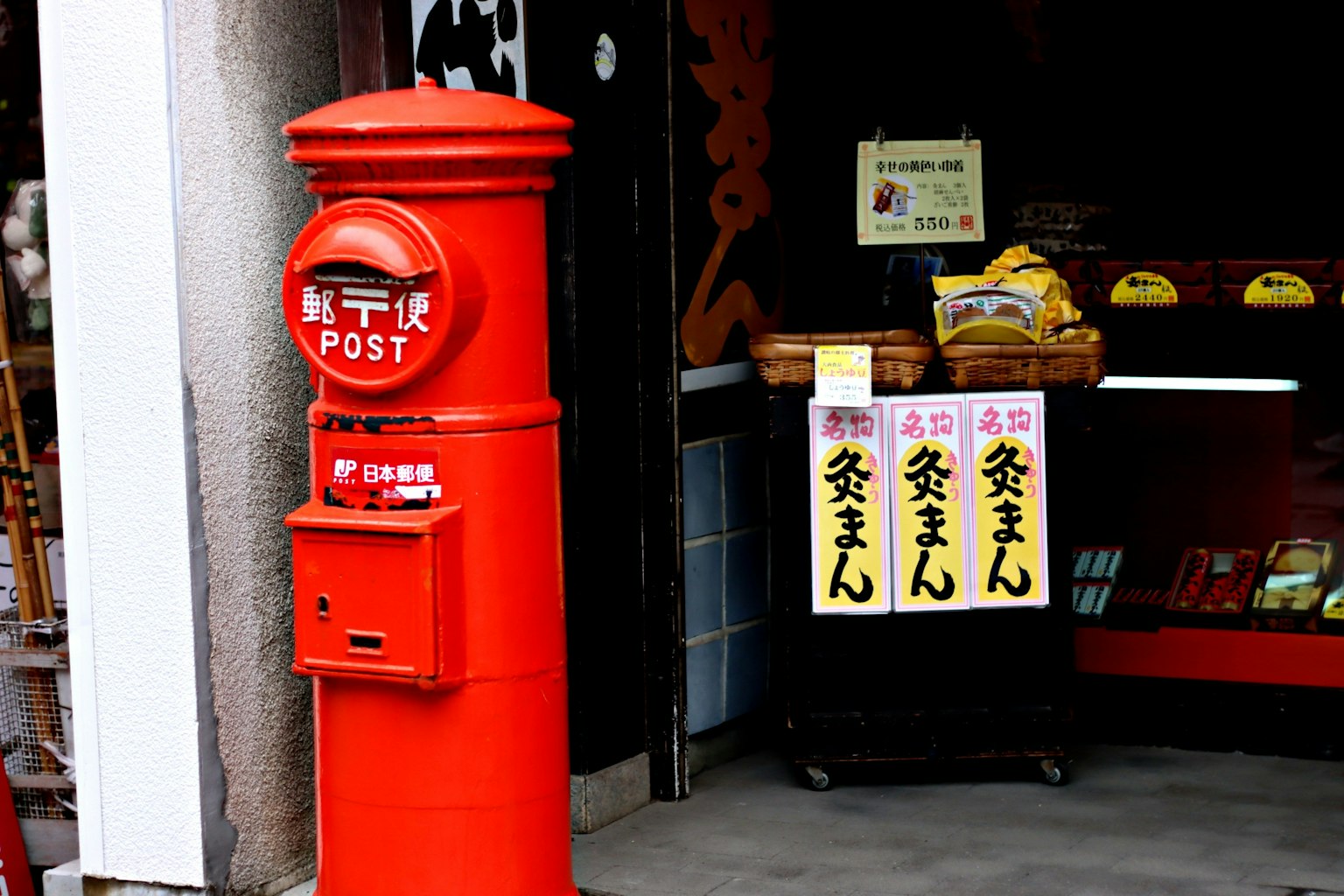Red mail post box with shop signs in the background