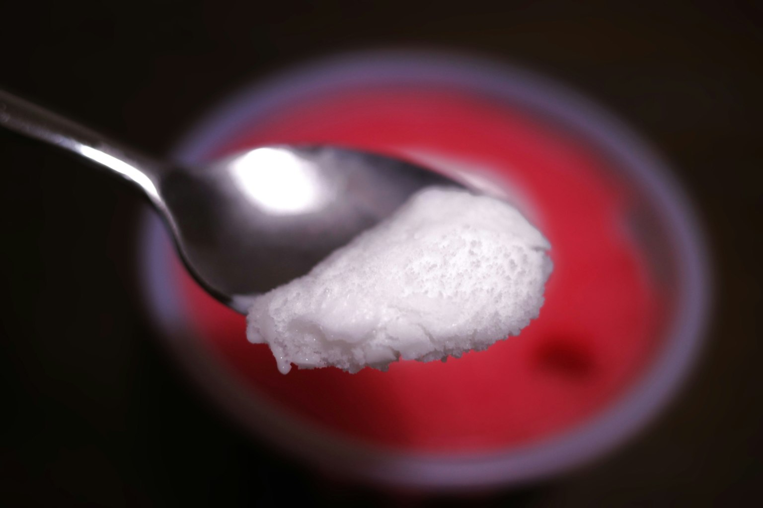 Ein Löffel mit weißer Creme über einem roten Dessert