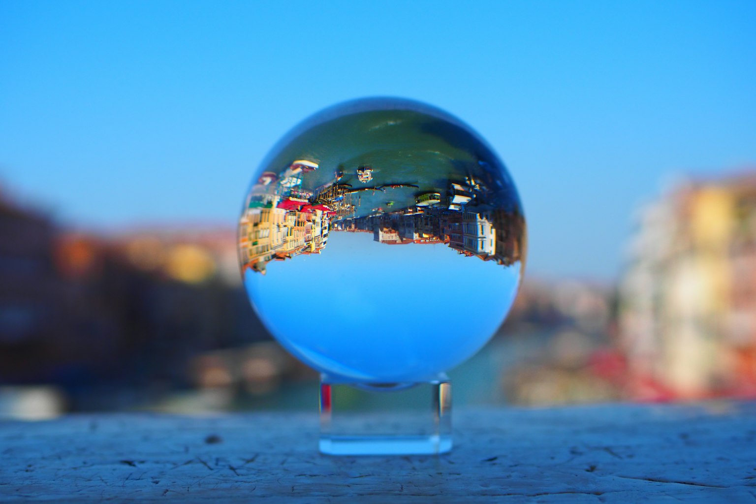Palla di cristallo che riflette un paesaggio vibrante con cielo blu e edifici colorati