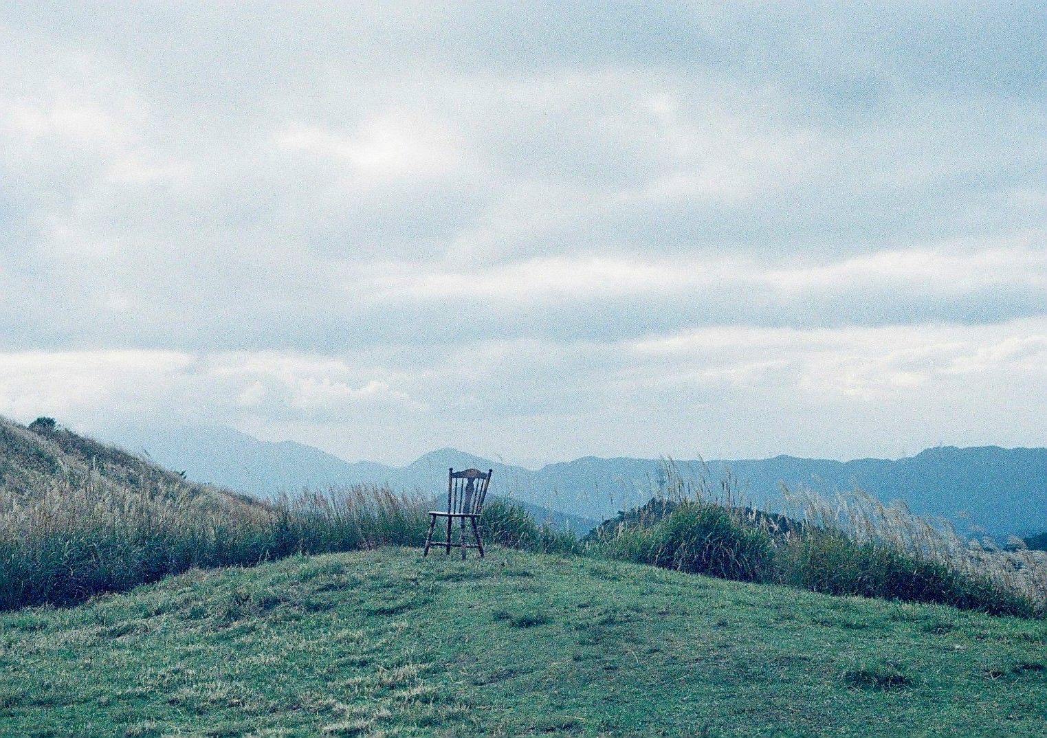 草地の上に立つ金属製の椅子と山並みの風景