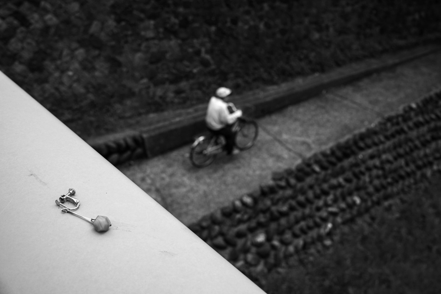 Black and white photo of a person riding a bicycle next to a stone wall