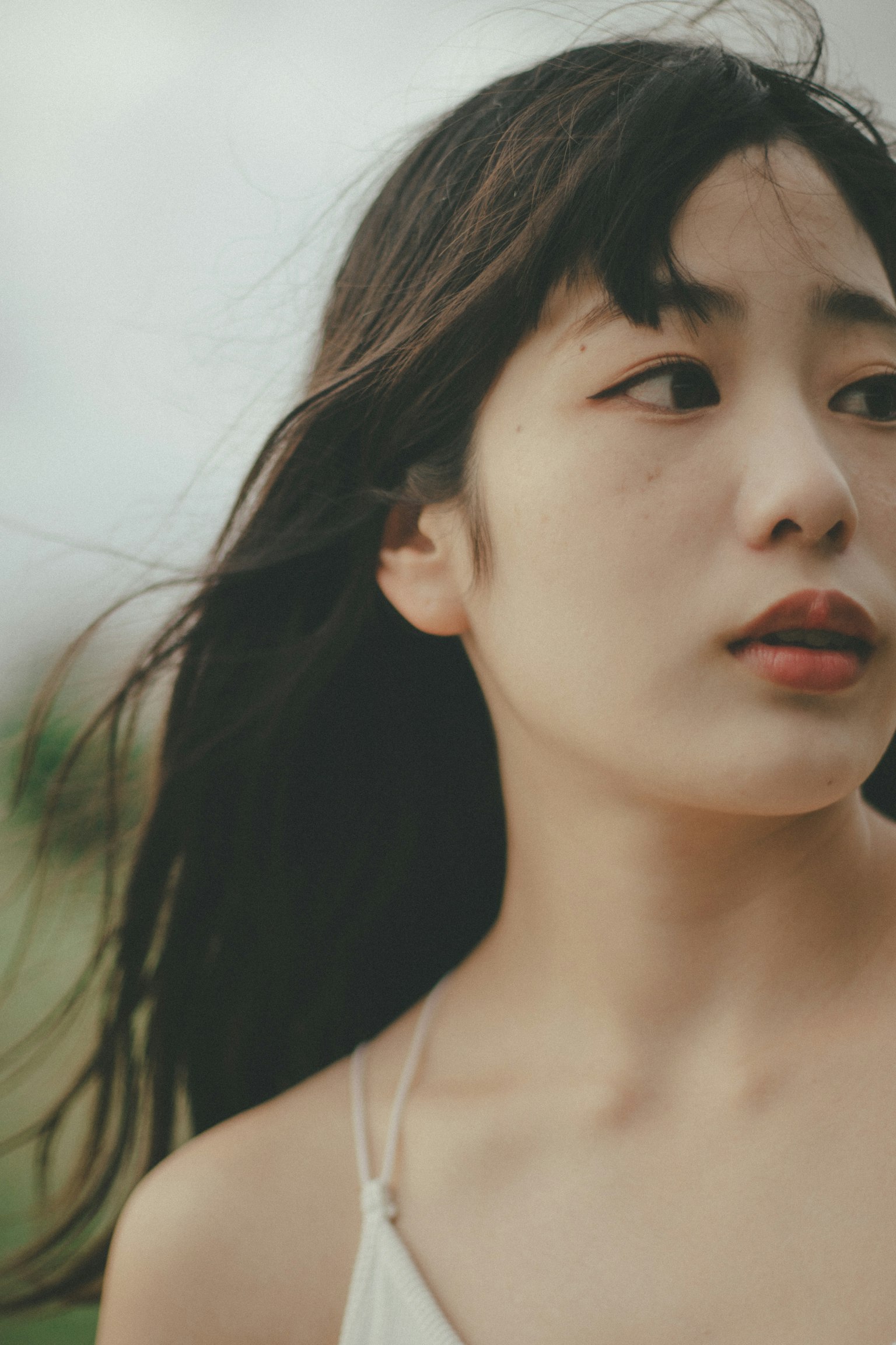 Profil d'une femme aux cheveux noirs flottants dans un cadre naturel avec une expression sereine