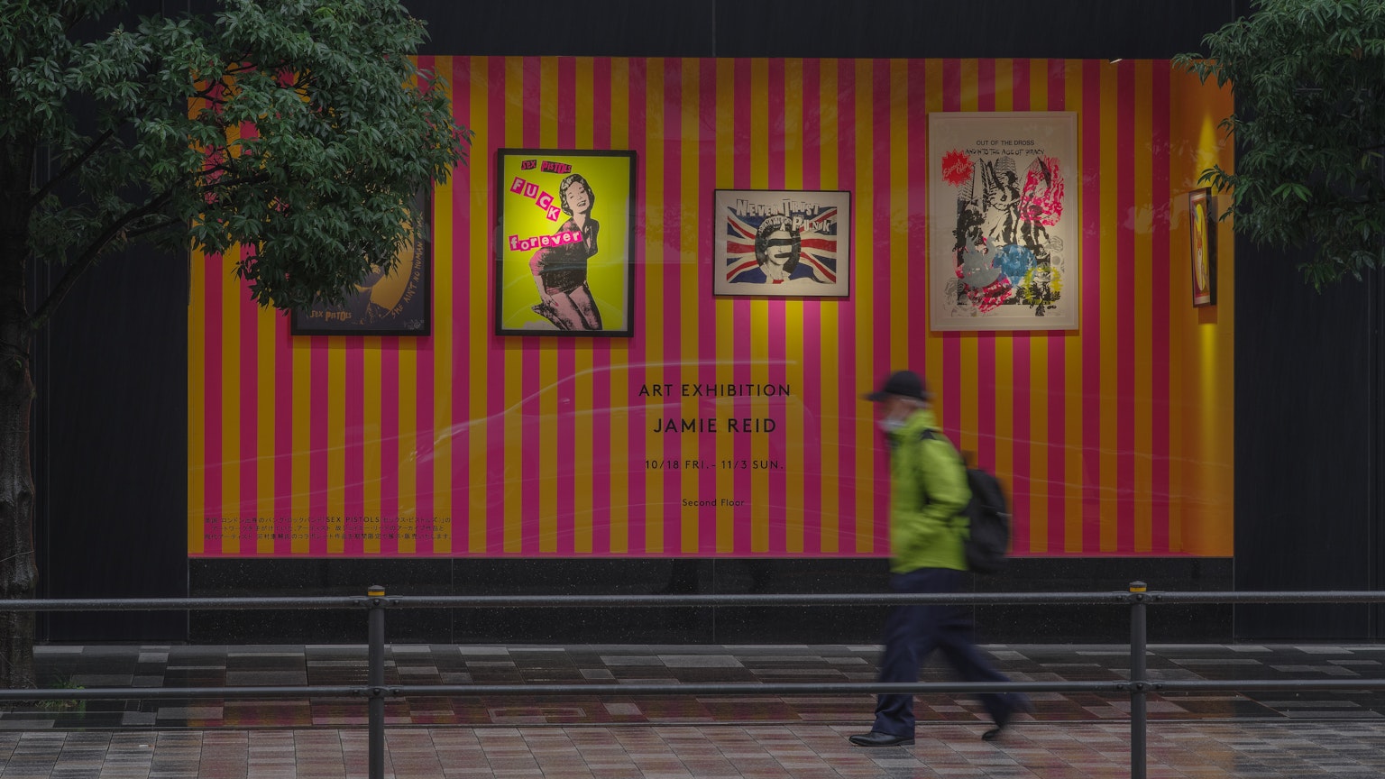 Une personne marchant sous la pluie avec des œuvres d'art sur un mur rayé coloré en arrière-plan
