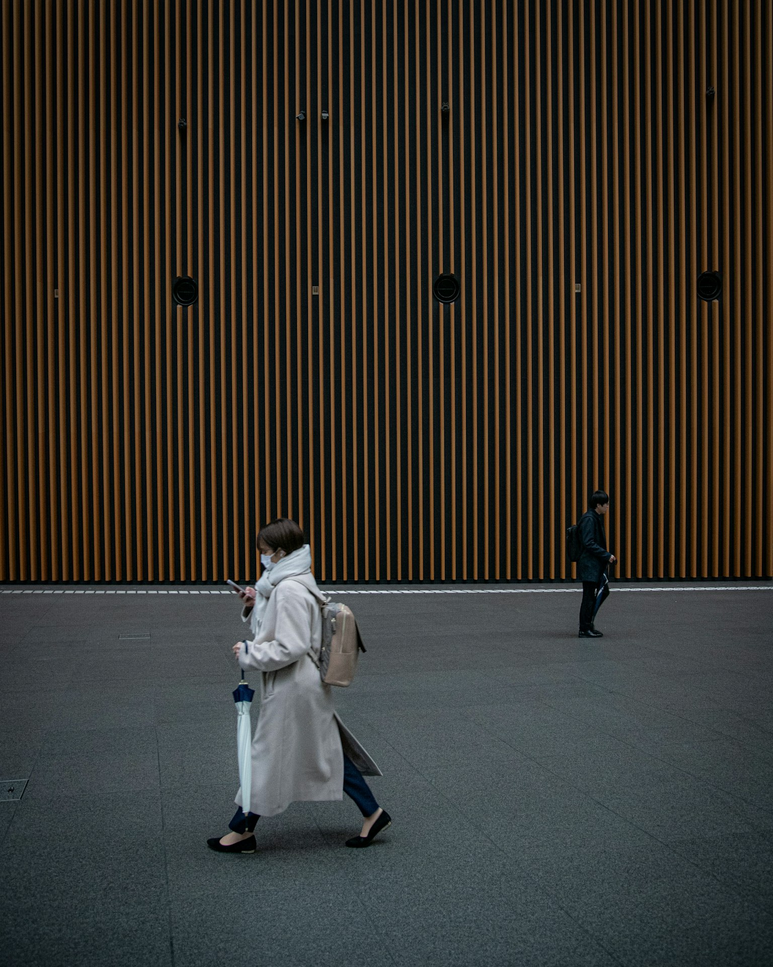 Una donna in un cappotto bianco che cammina davanti a un muro a strisce in legno