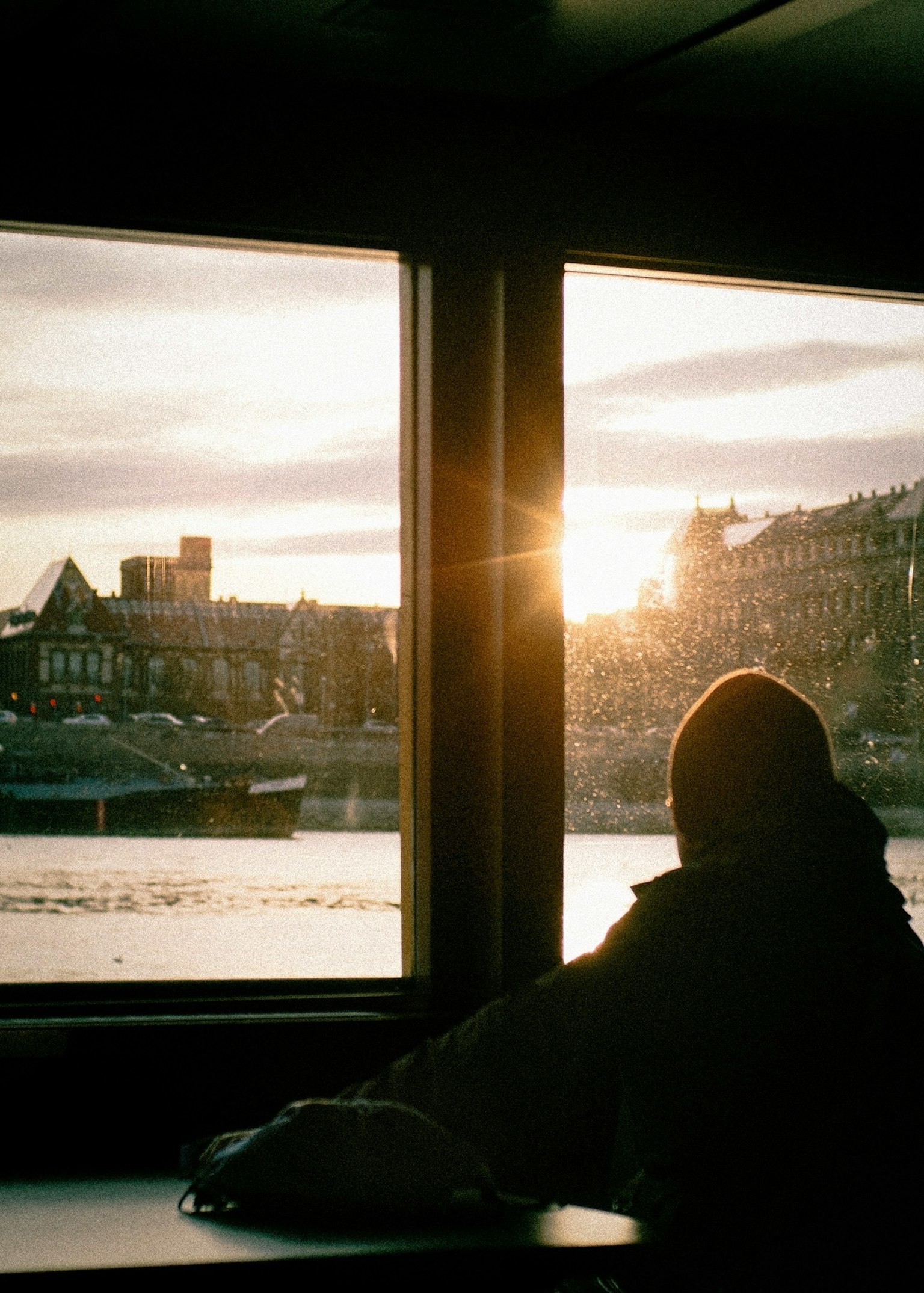 Persona mirando el atardecer a través de la ventana con vista al río