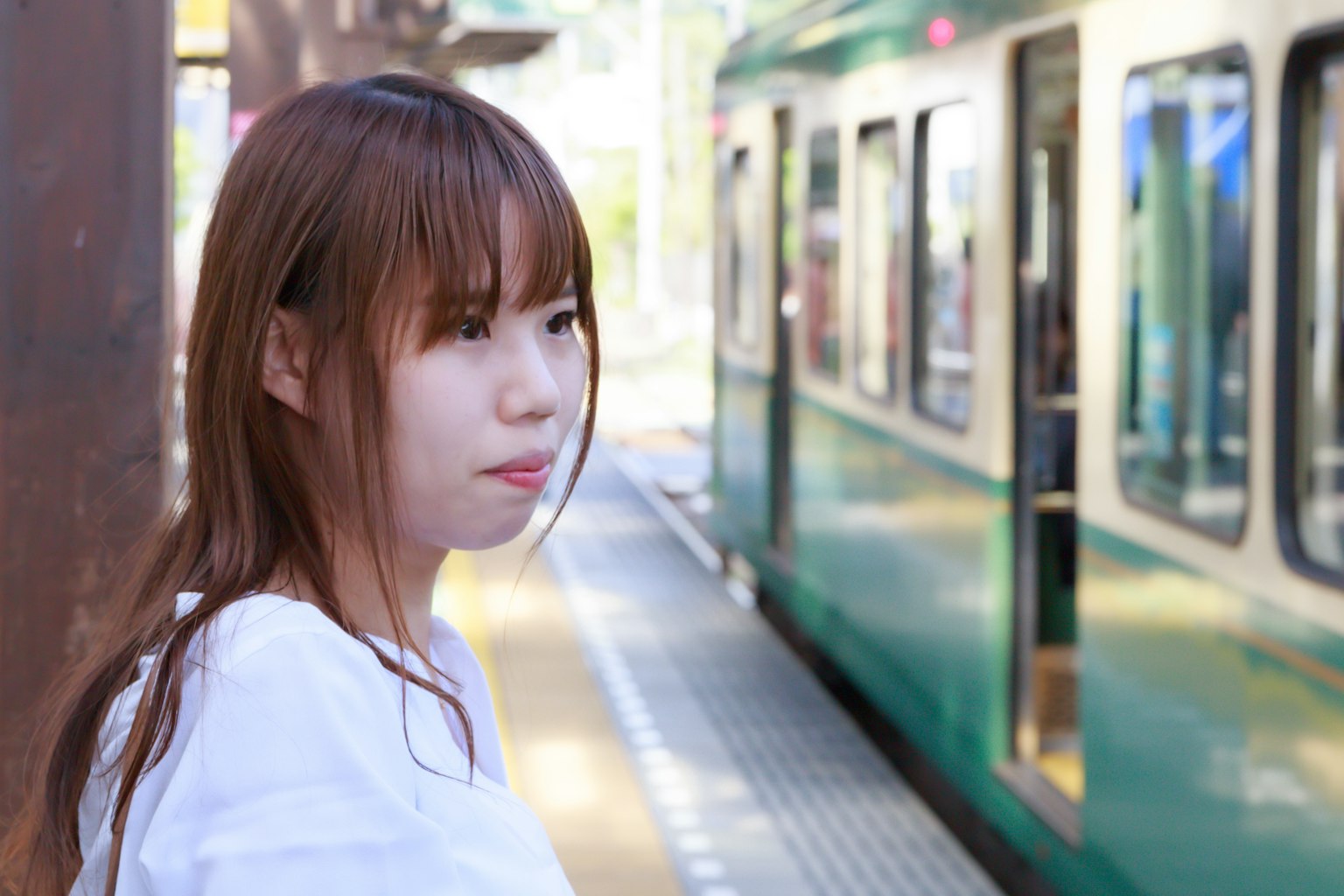 A woman waiting at a train station near a green train