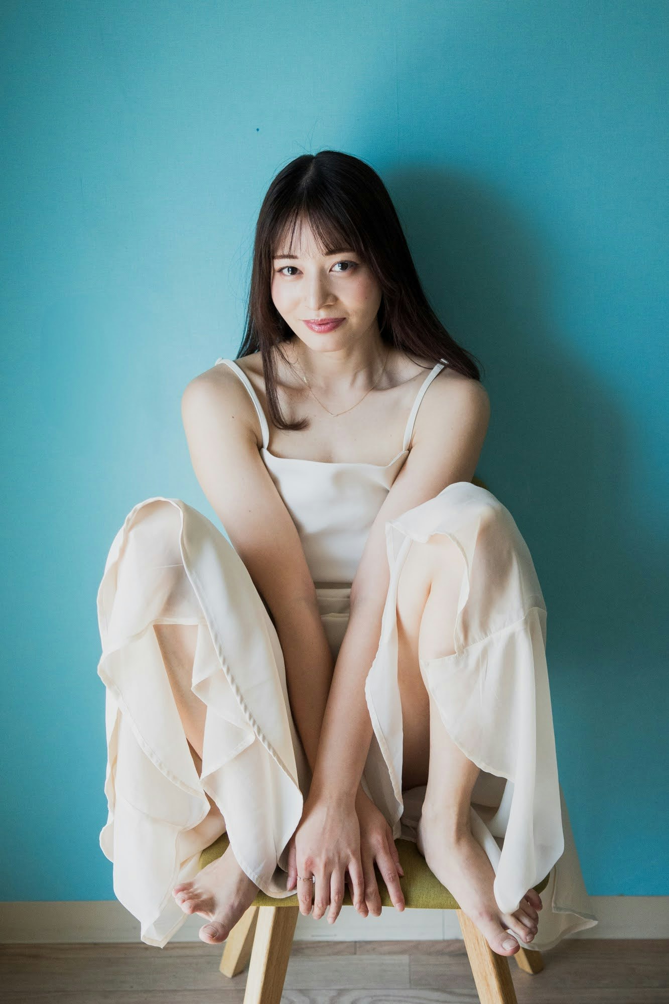 青い背景の前で白いキャミソールの女性が椅子に座っている