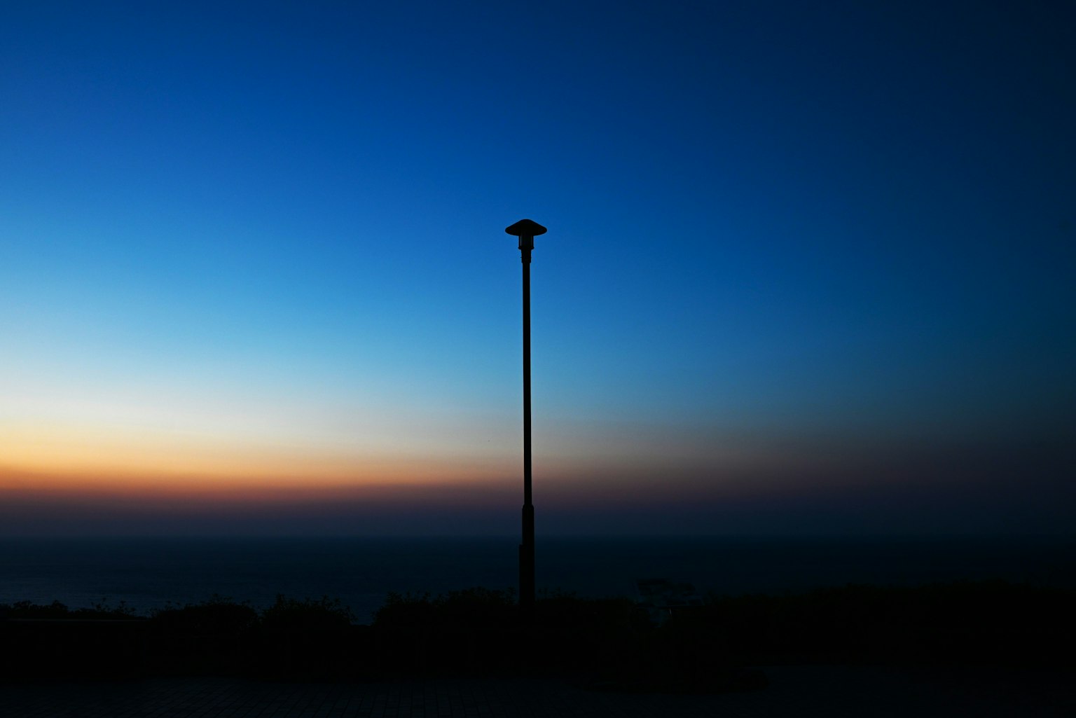 Silhouette di un lampione contro un cielo blu e un tramonto arancione