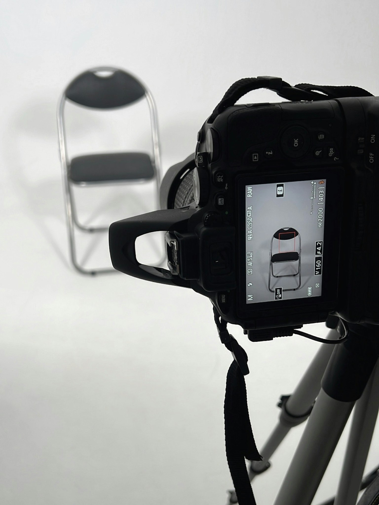 Kamera yang difokuskan pada kursi hitam dengan tripod dan latar belakang cerah