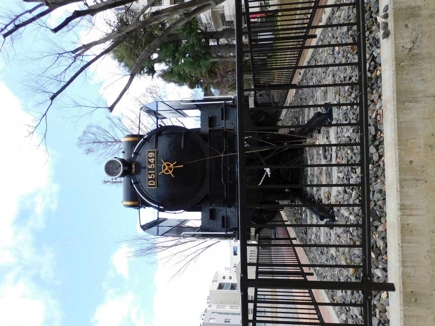 Black steam locomotive by the tracks with a metal fence