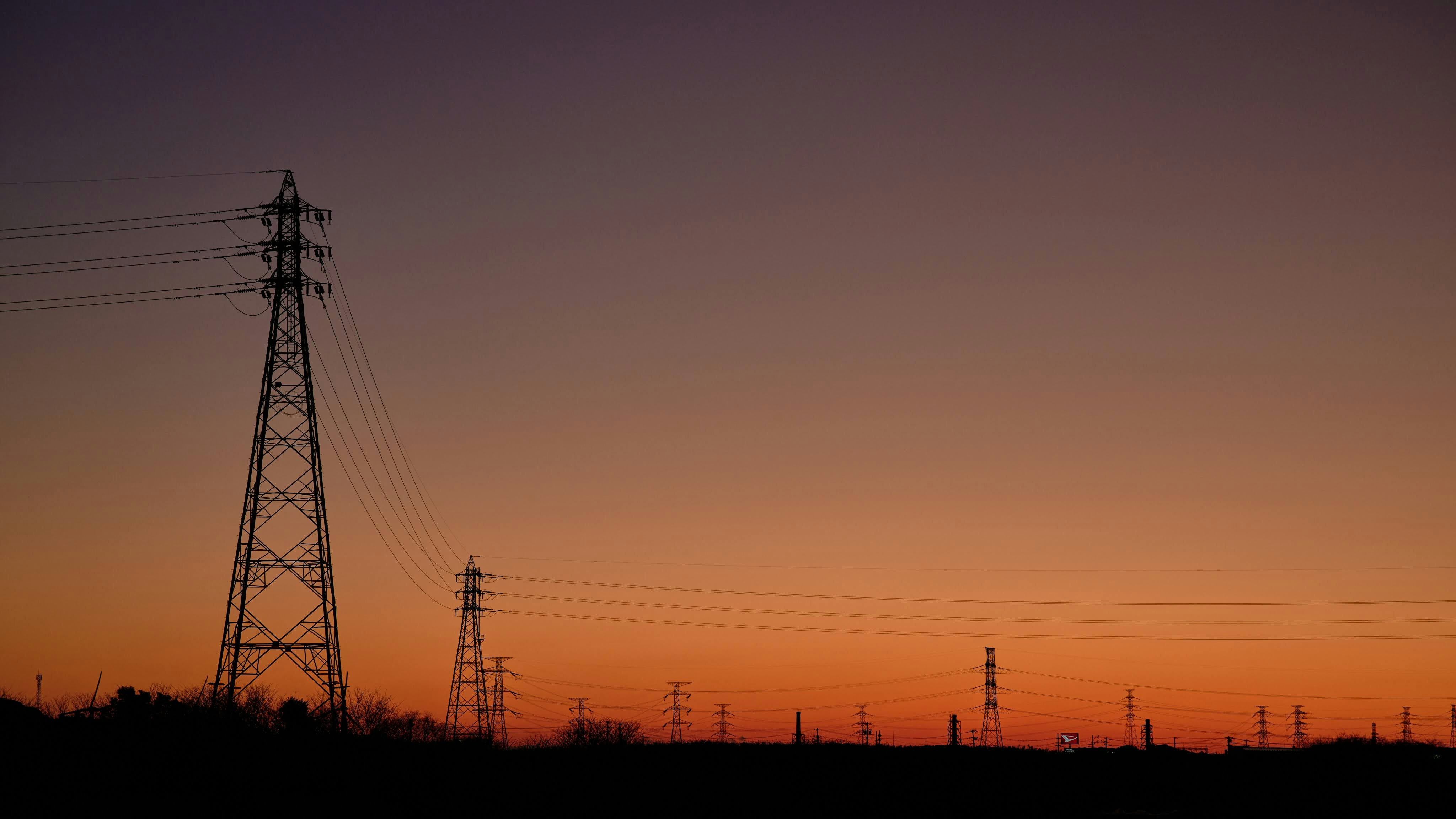 夕焼けの空に伸びる送電鉄塔と電線