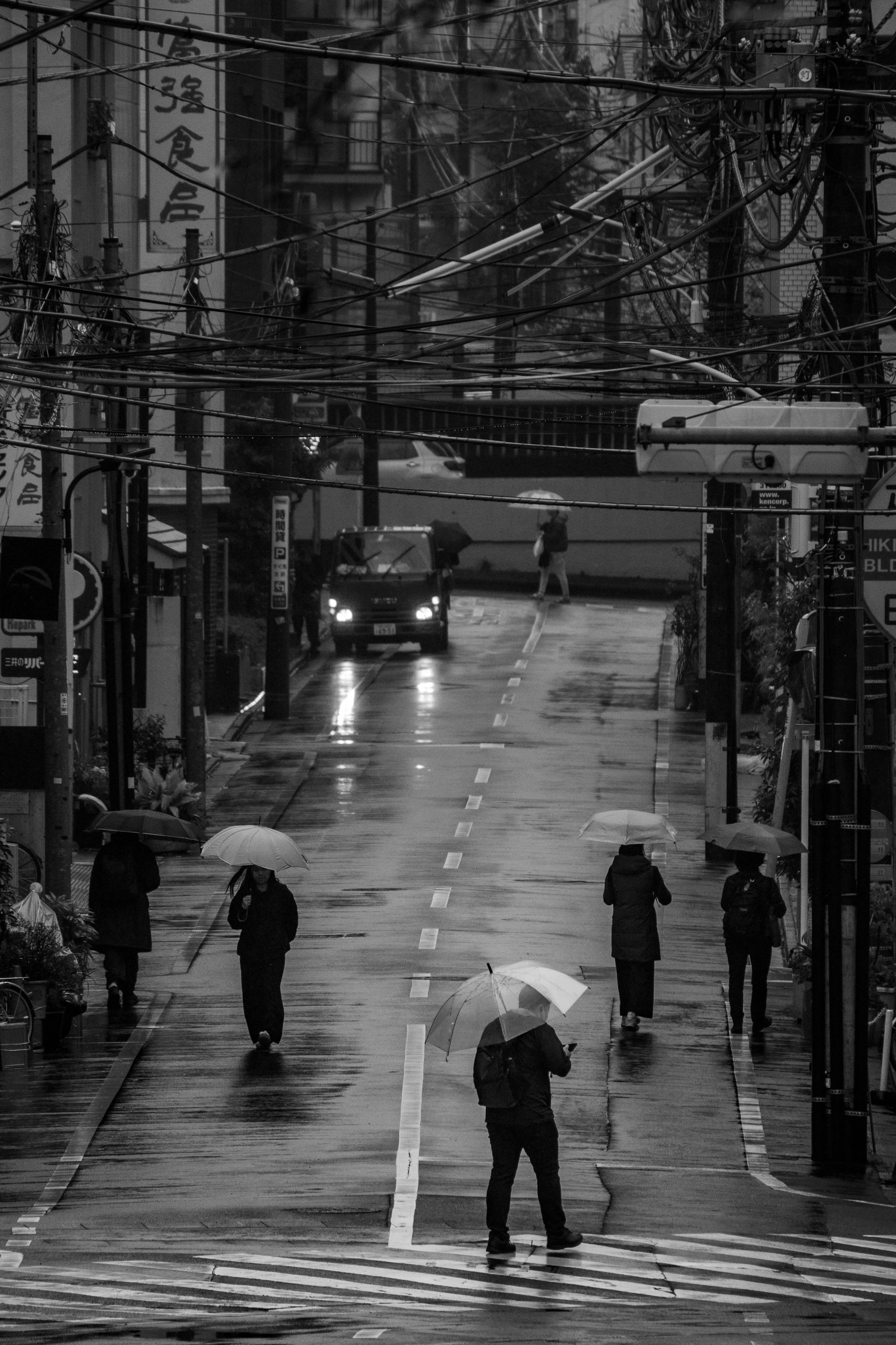 雨の路地に並ぶ横断歩道と電線のある街並み