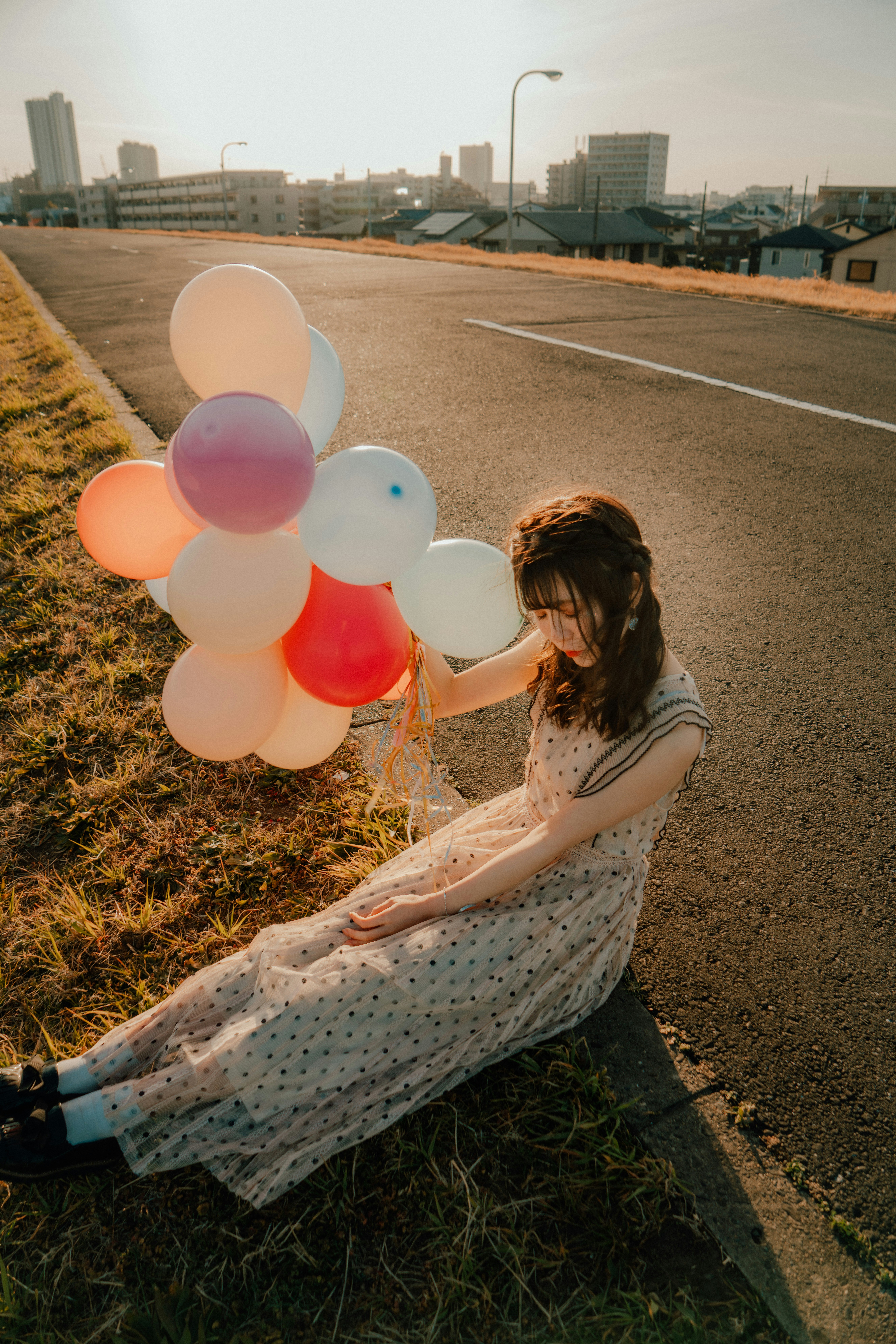 A child holding balloons on grass beside a park walkway