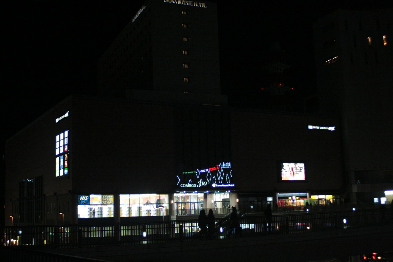Exterior of a commercial building at night featuring bright signs and shop windows