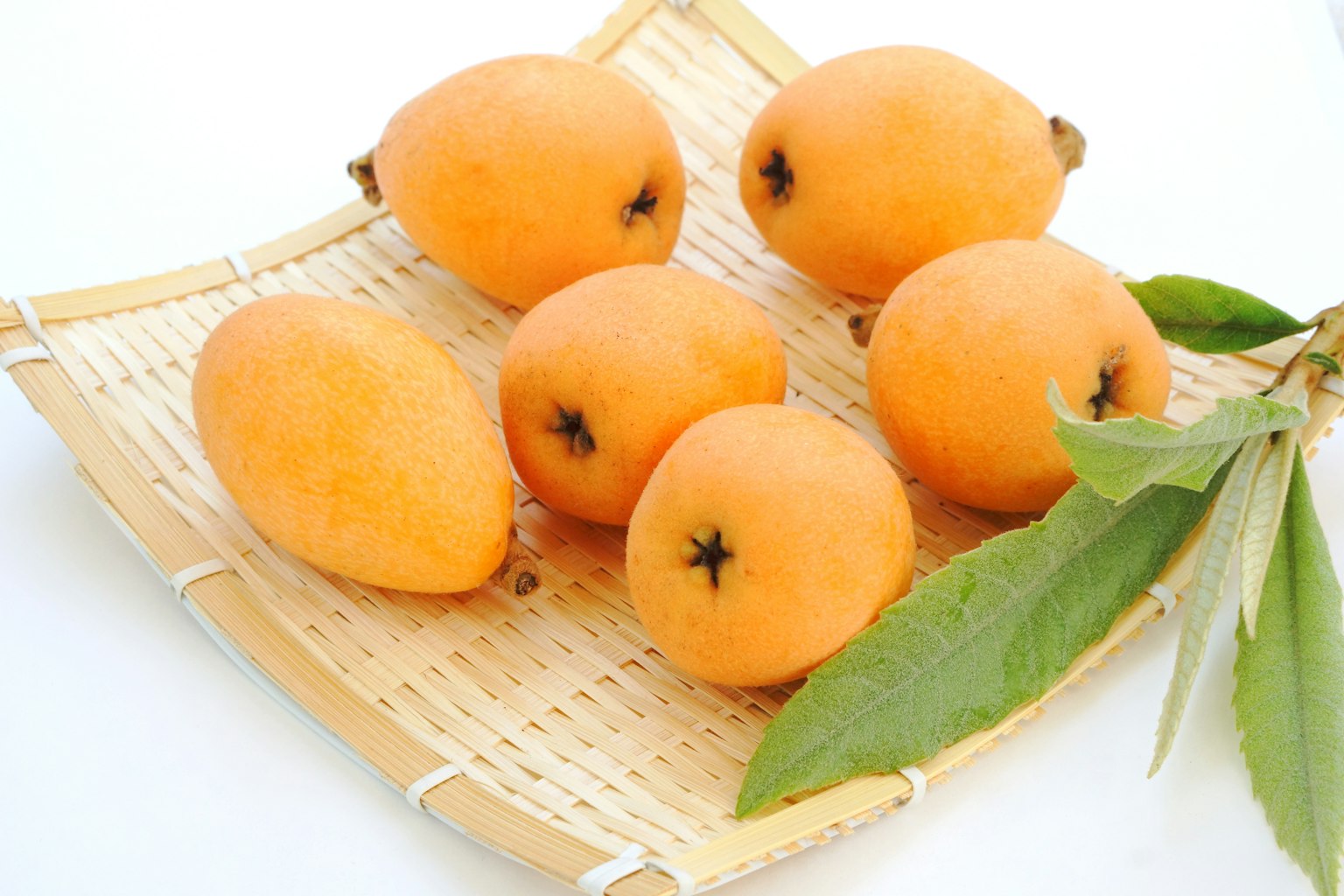 A basket containing several ripe loquats with green leaves