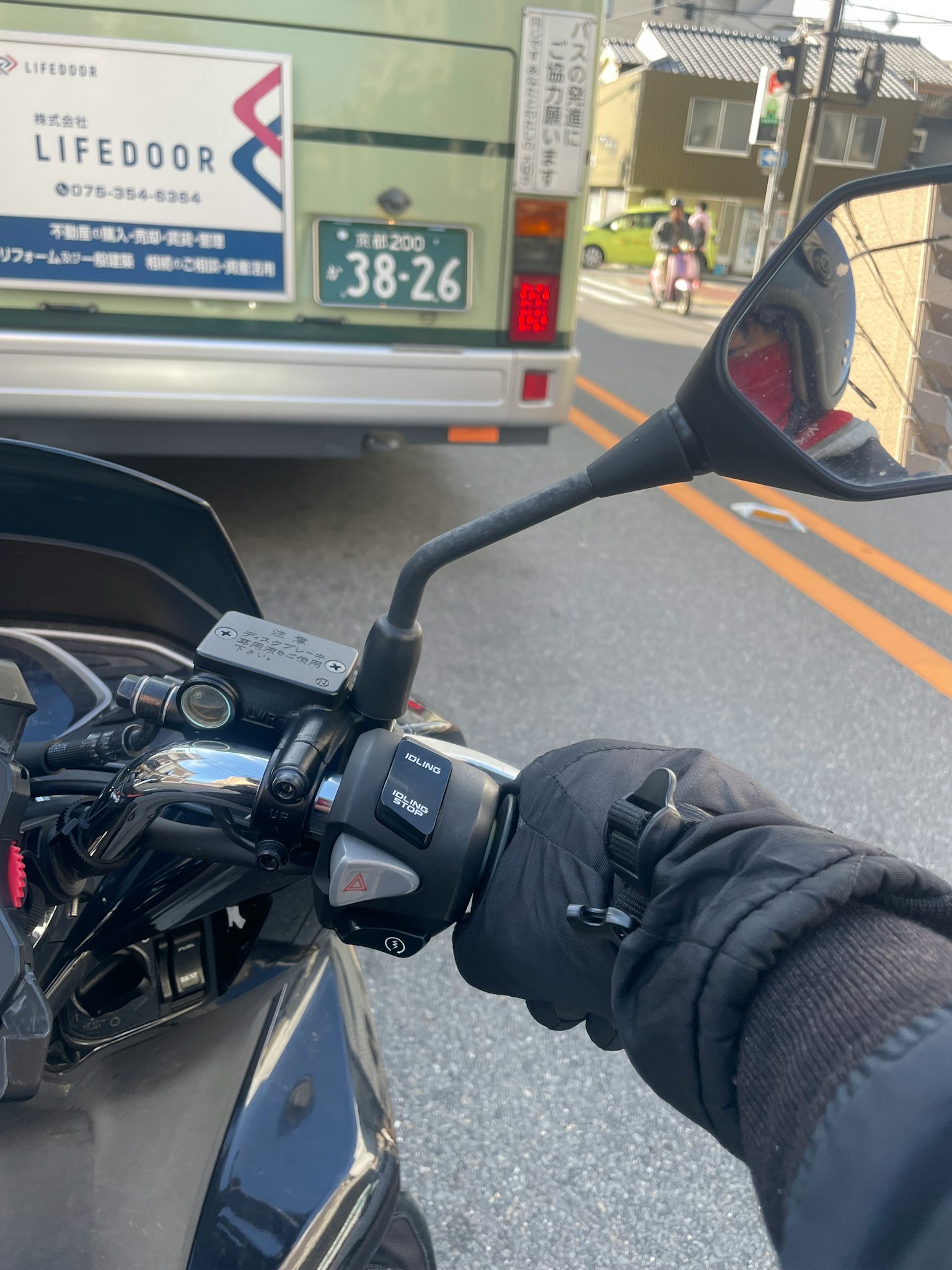 握住摩托車把手的手的特寫，背景中有一輛公車