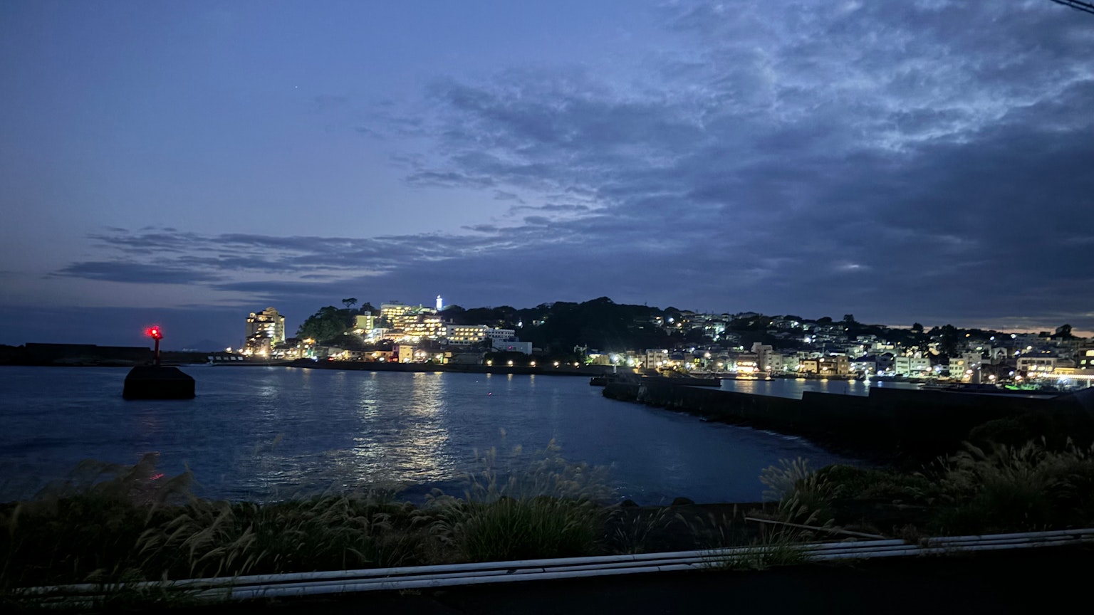 Hermosa vista nocturna de una ciudad costera con reflejos iluminados en el agua y un cielo nublado