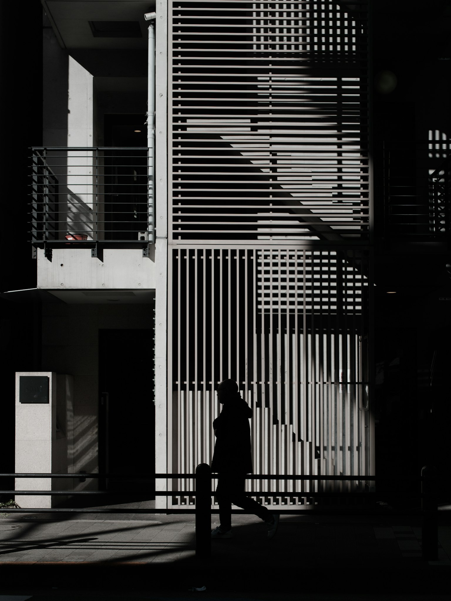 Silhouette of a person walking beside a striped building casting shadows