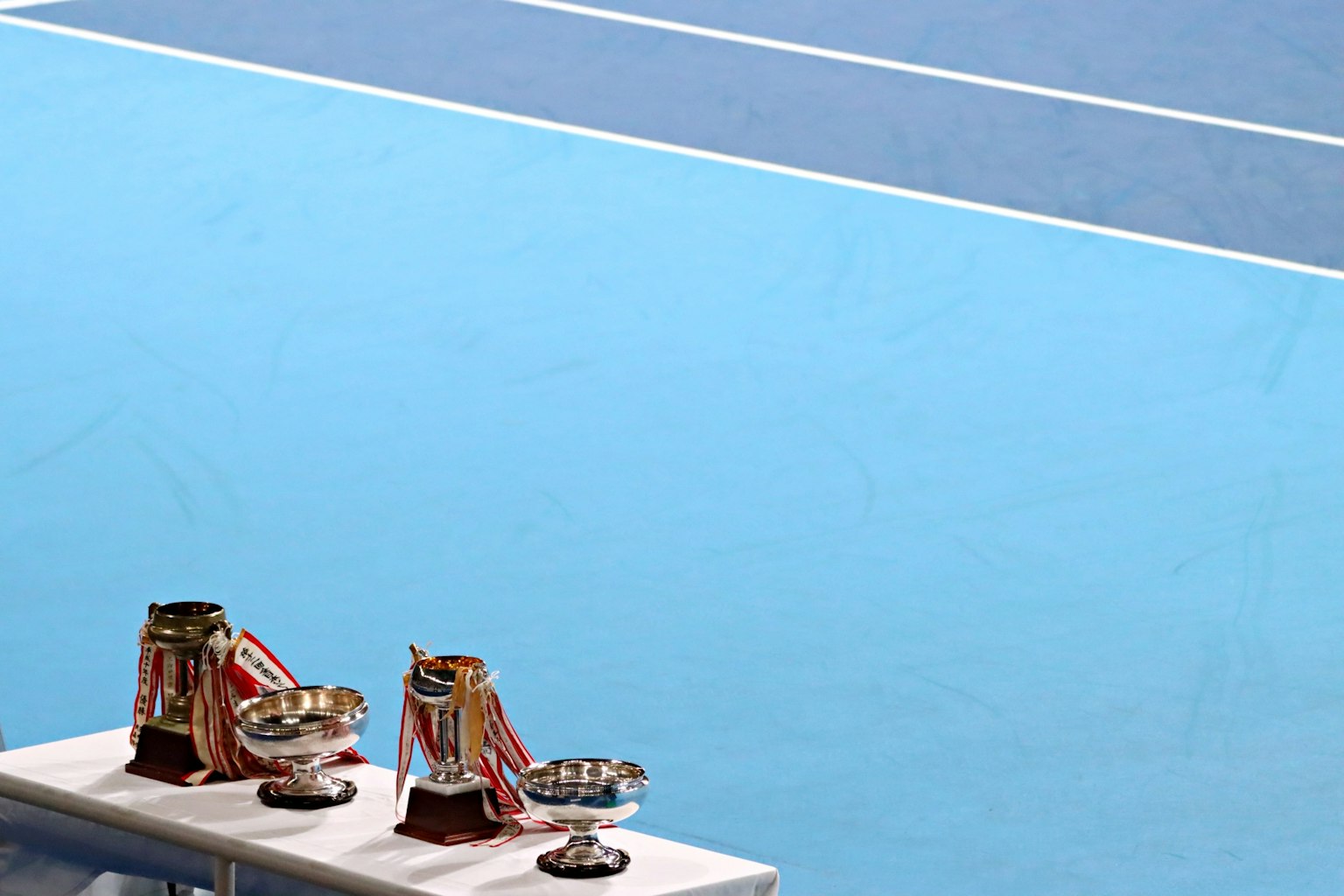 Trofei e coppe esposti su un tavolo accanto a un campo da tennis blu