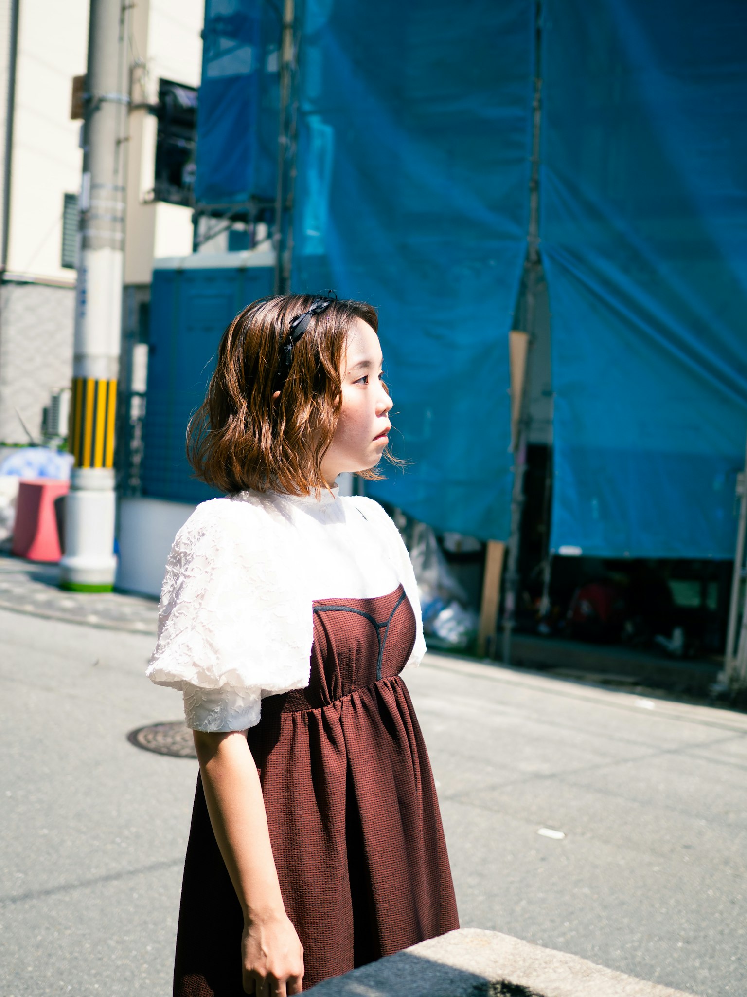 青い布の背景の前に立つ女性の横顔　茶色のドレスと白いブラウス　街の風景