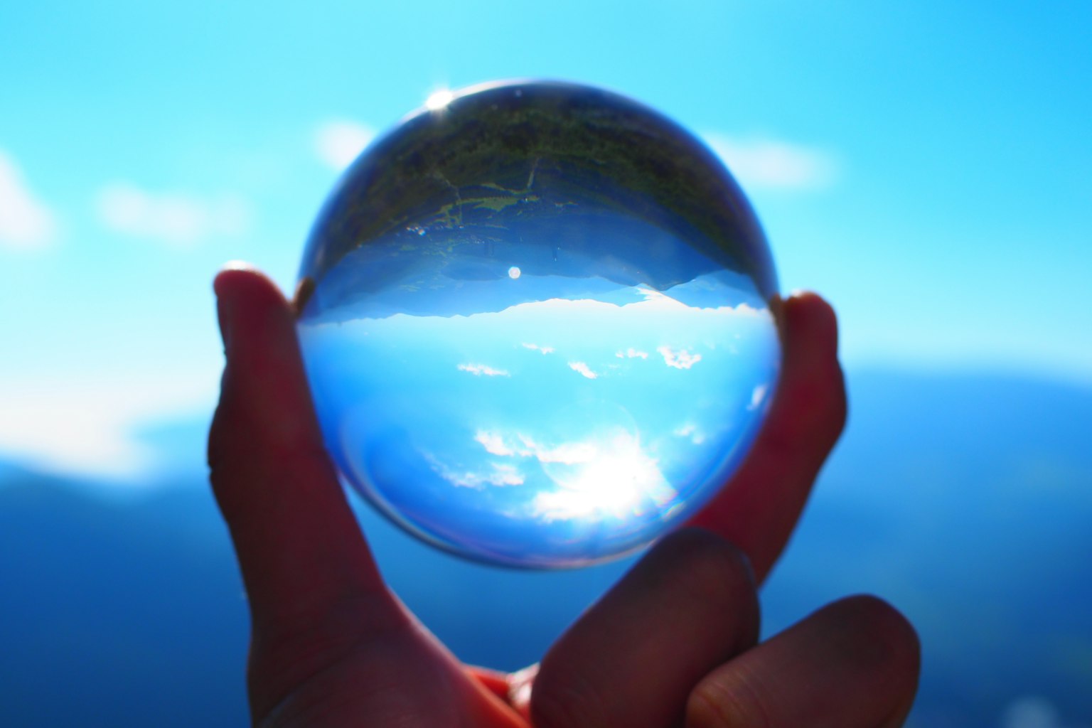 Mano che tiene una sfera di cristallo che riflette un cielo blu