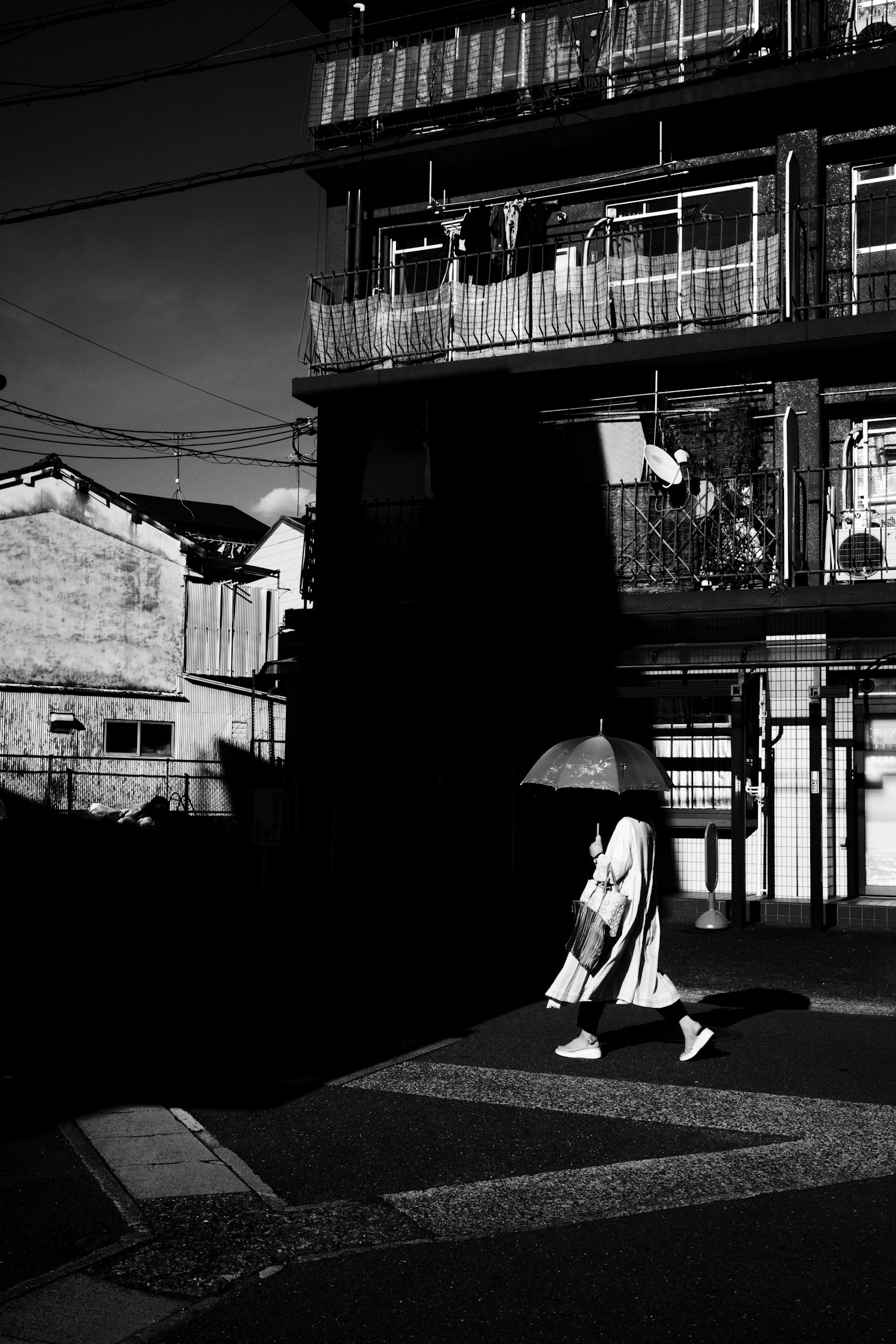 Una persona in abiti bianchi con un ombrello che cammina in una scena urbana in bianco e nero
