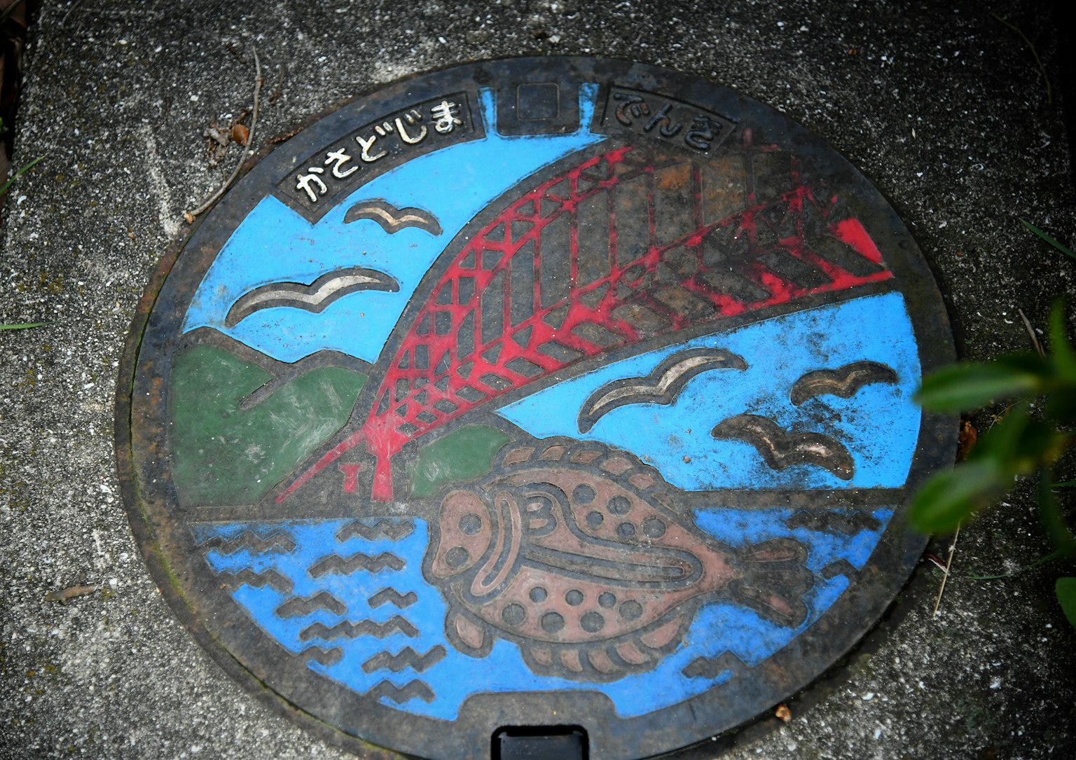 Tapa de alcantarilla con un pez y un puente rojo sobre un fondo azul