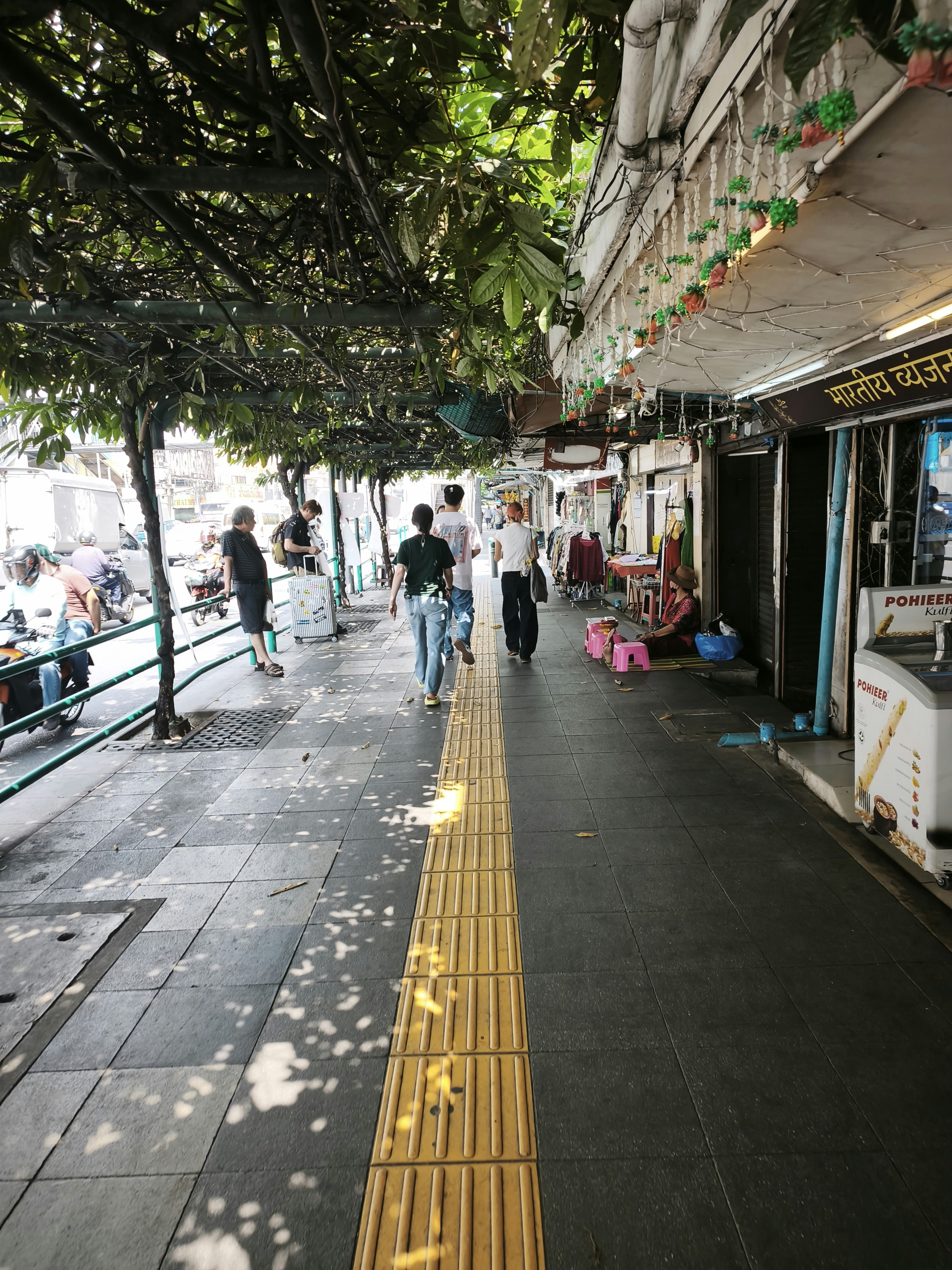 木陰の並木道と商店街の軒先を歩く人々